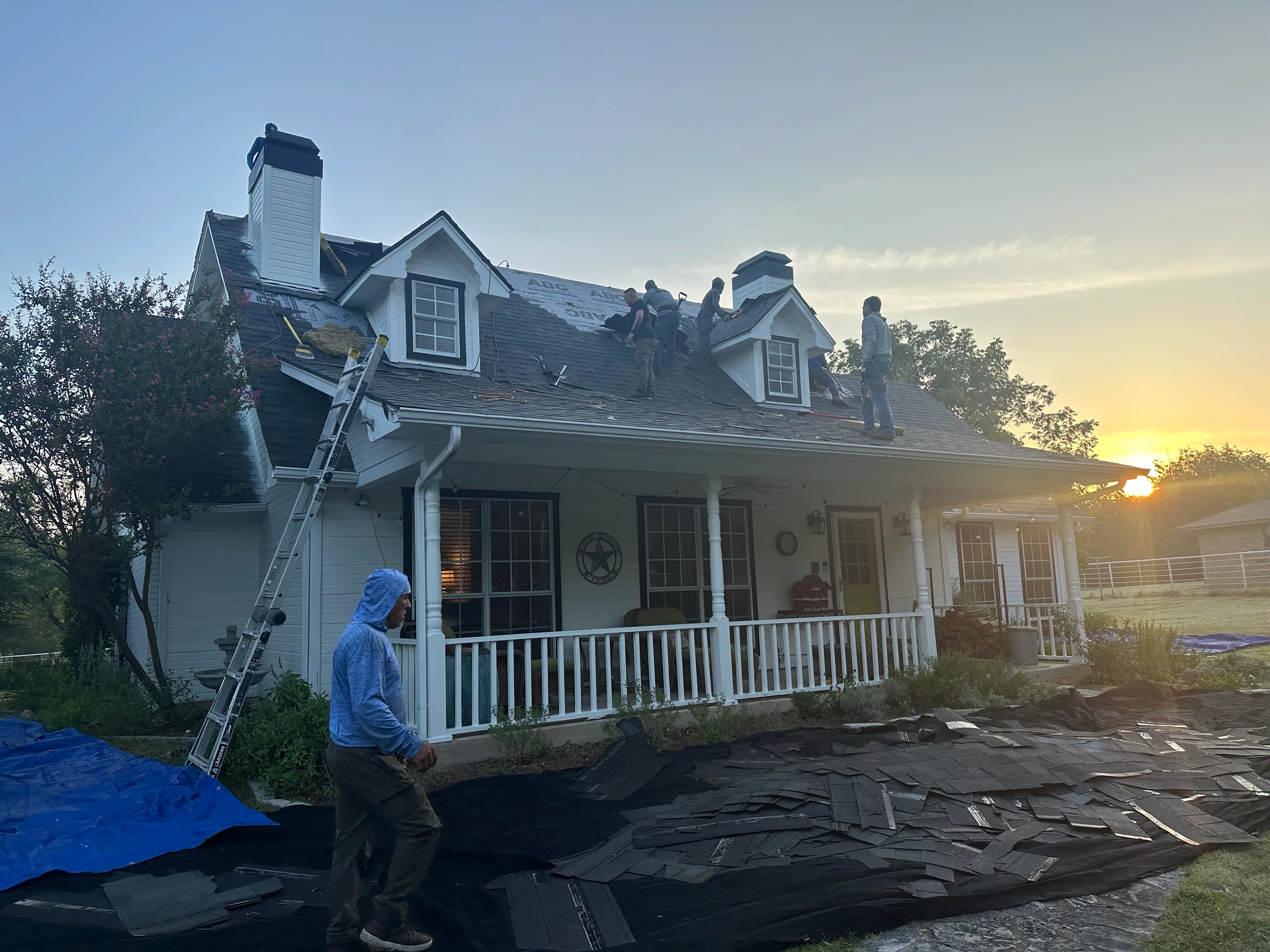 Roofers installing new shingles on two-story home with dormers and white trim