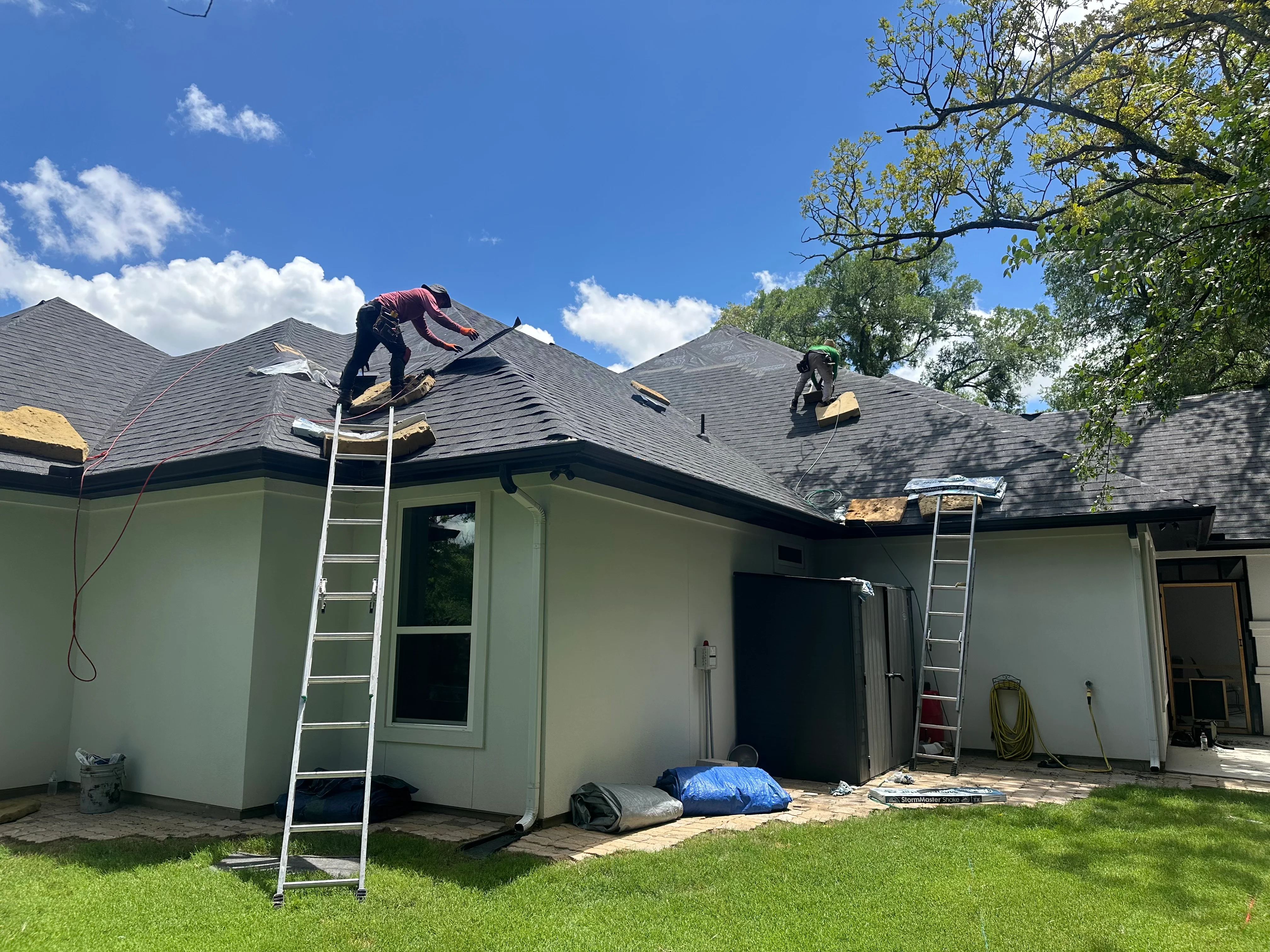 Roofers installing gray architectural shingles on multi-pitched residential roof with exposed decking