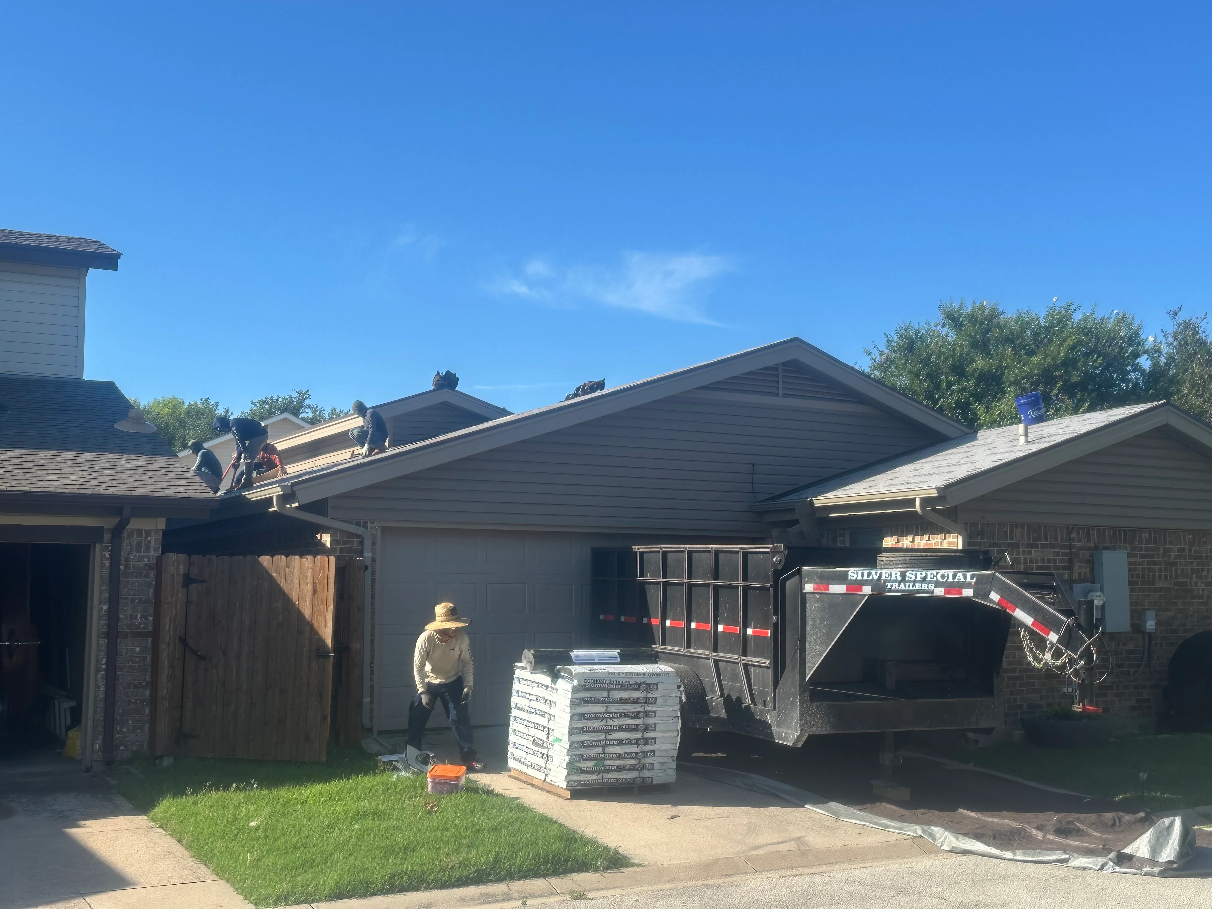 Roofers installing asphalt shingles on residential gable roof with material delivery trailer