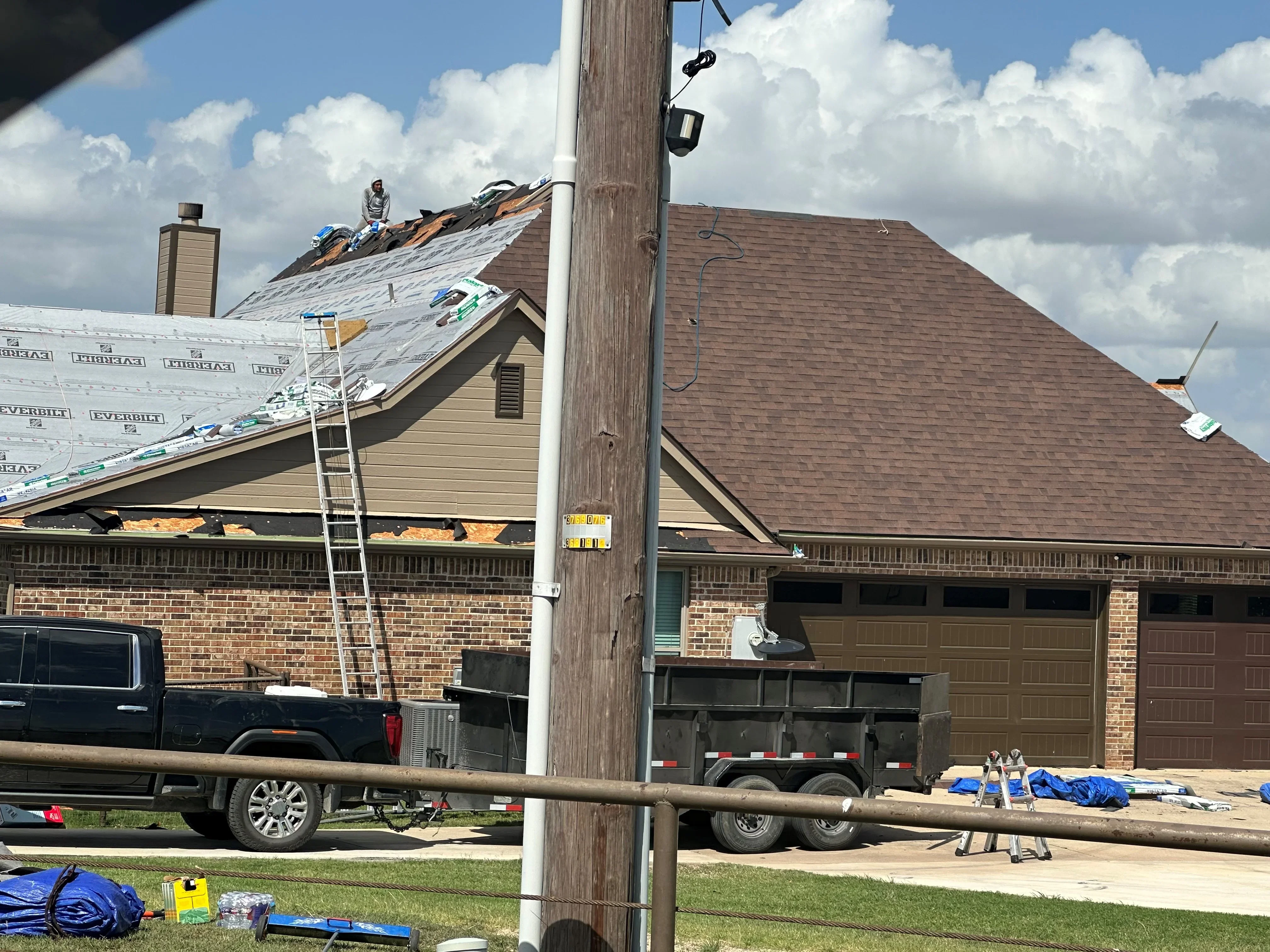 Roofer installing brown architectural shingles on residential home with brick exterior