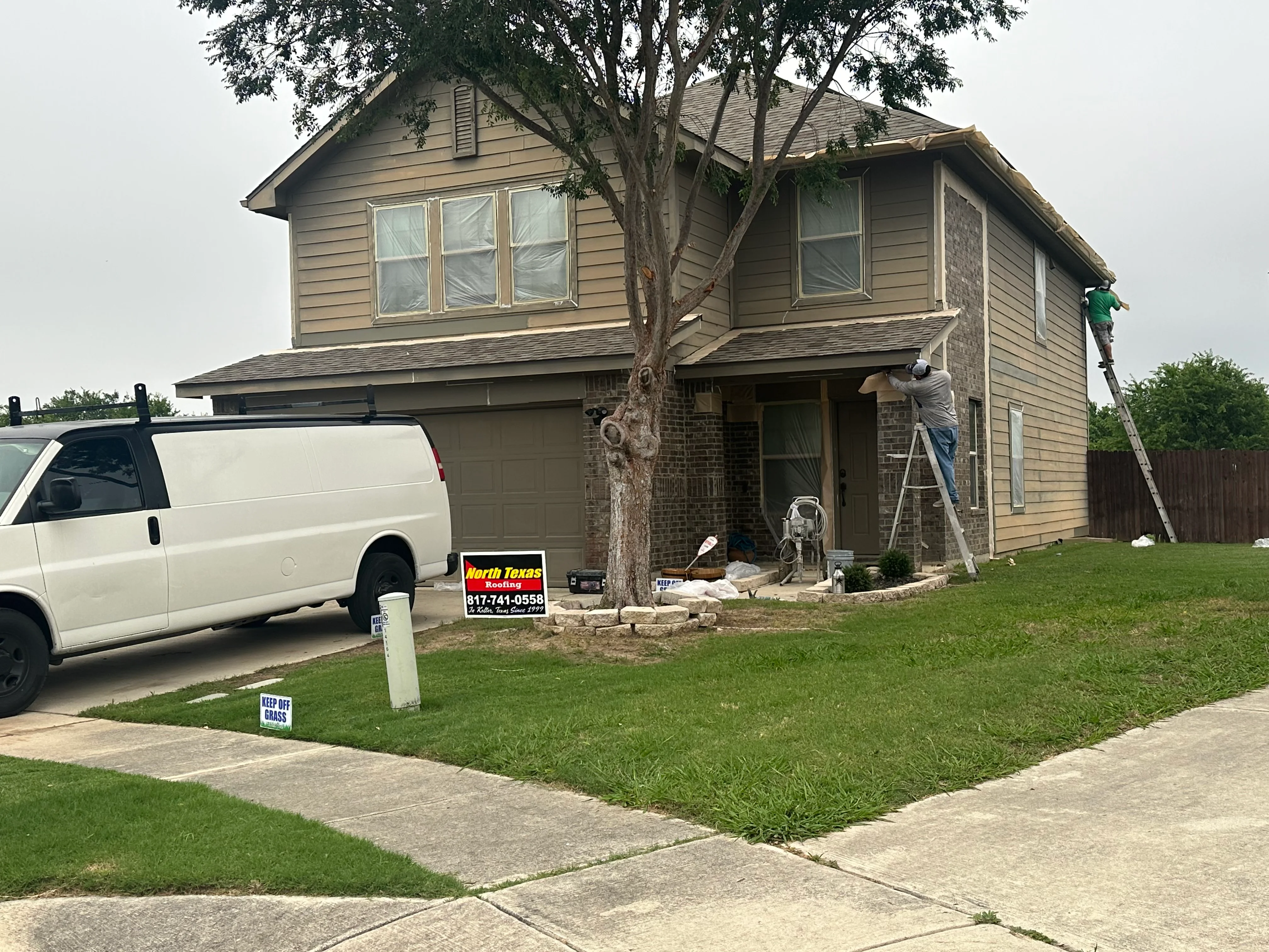 Two-story home with asphalt shingle roof, technician on ladder performing roof inspection and maintenance work