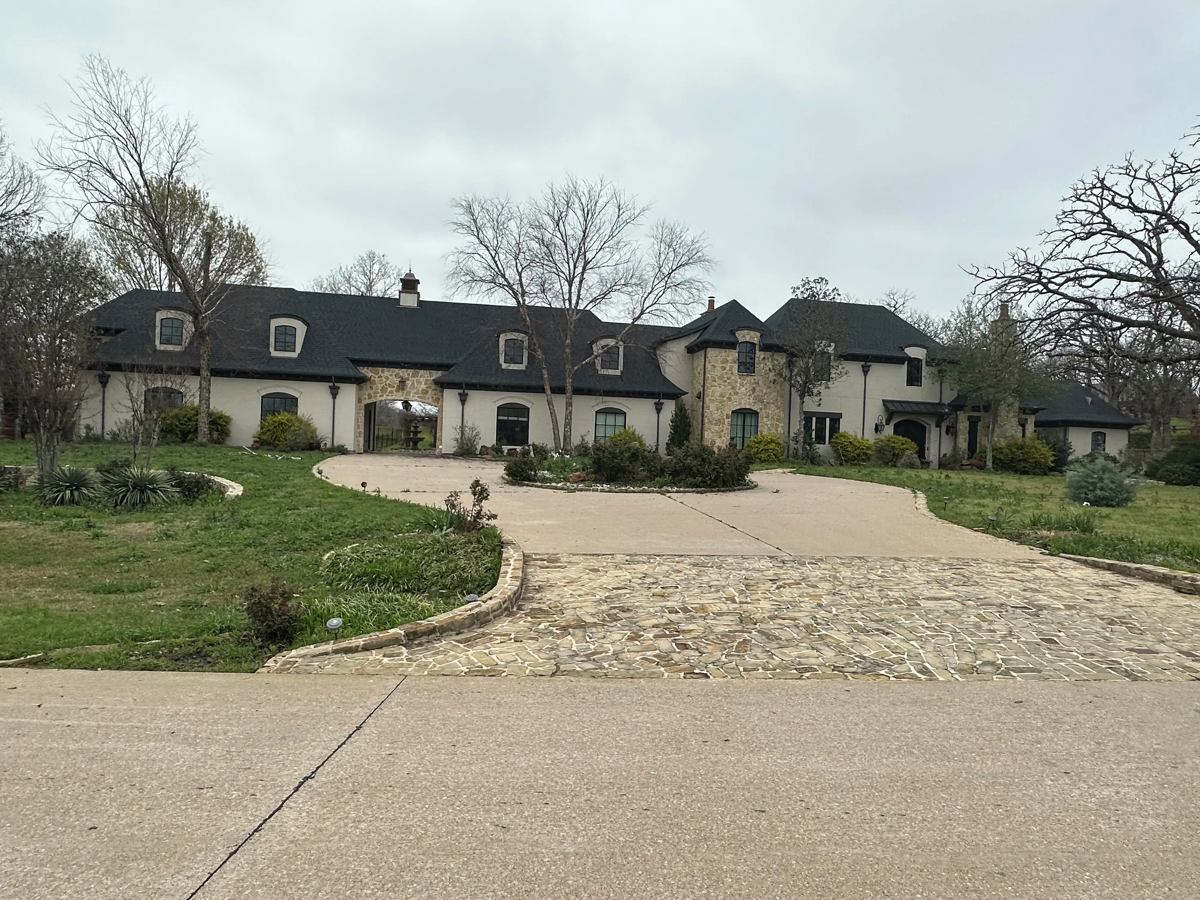 French Country home with dark architectural shingles, multiple dormers, and complex roofline