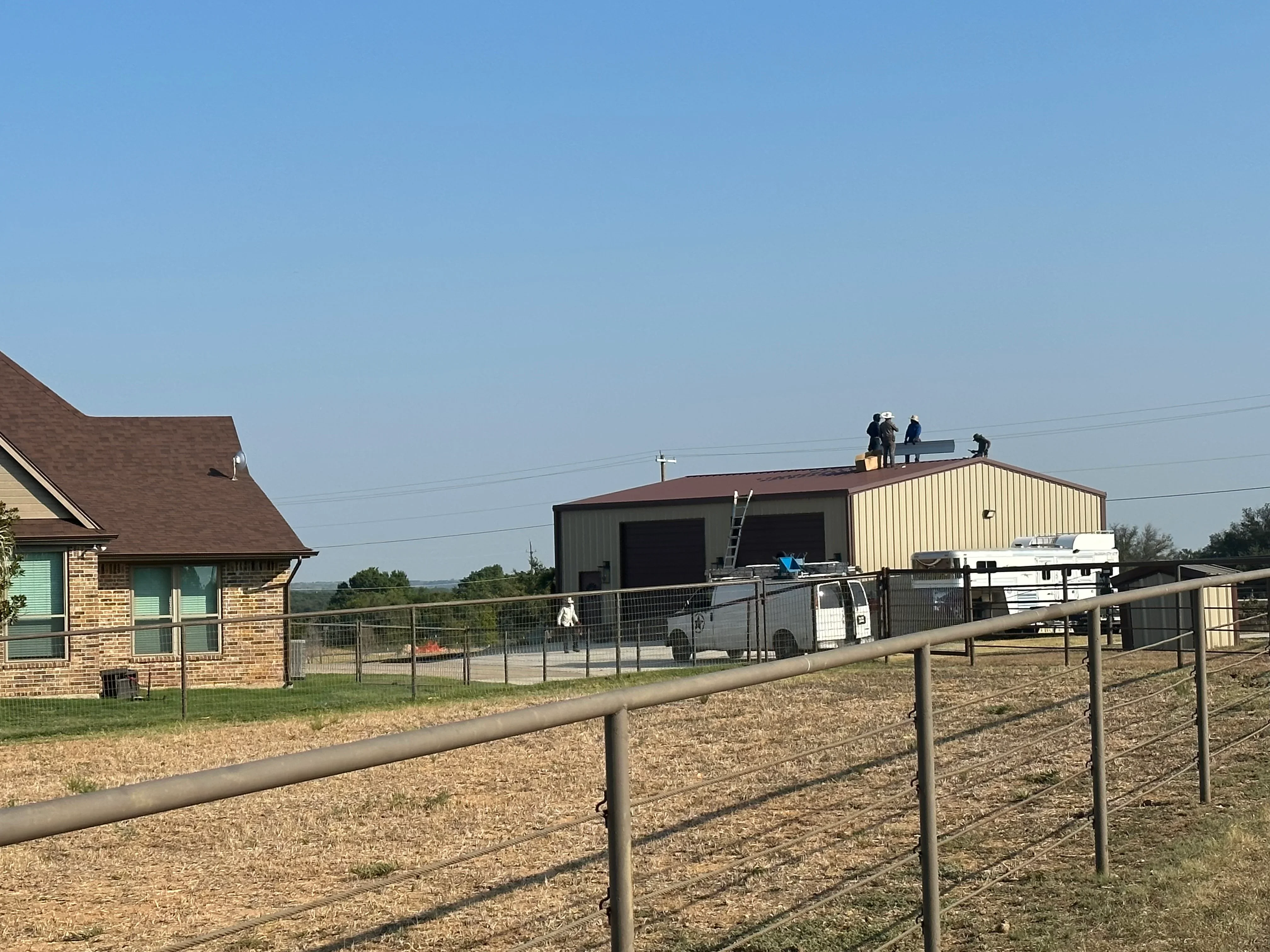 Metal roof installation on agricultural building with standing seam metal roofing in rust and cream colors