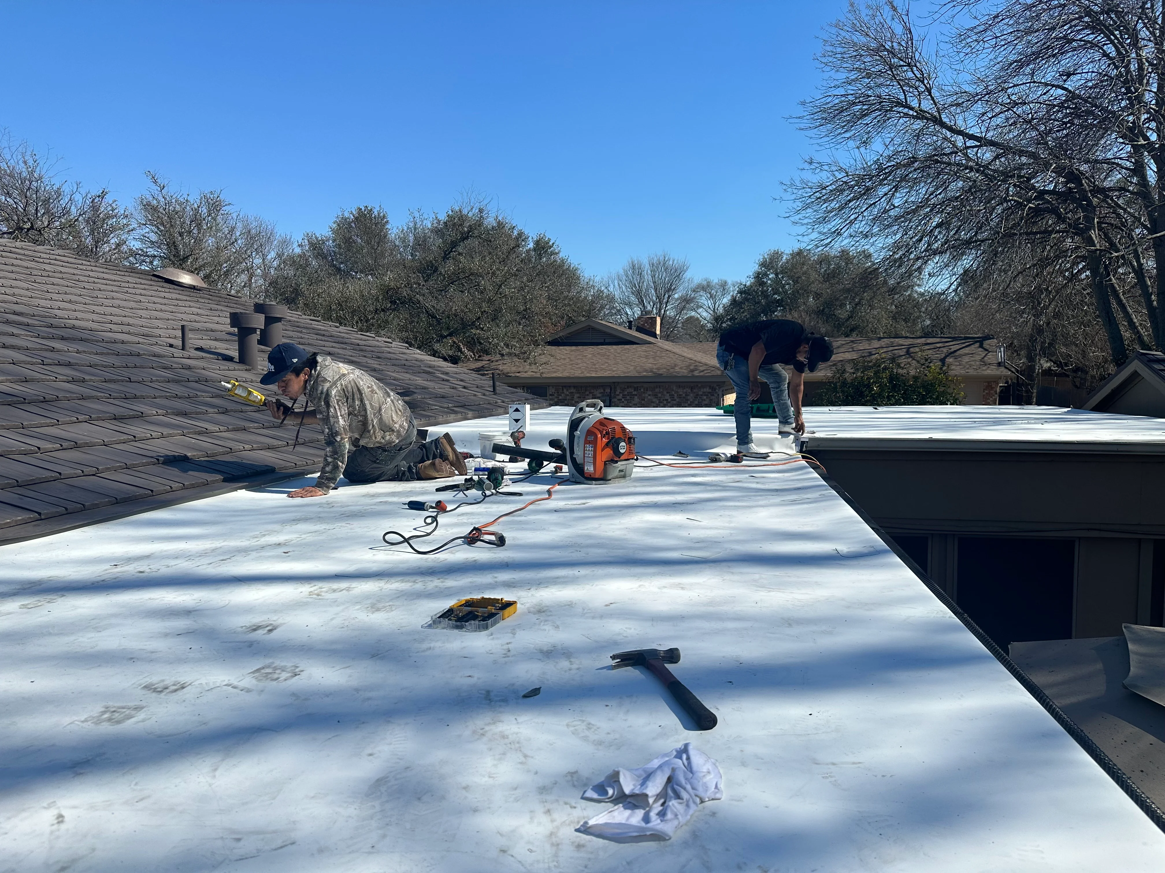 Workers installing white TPO membrane on flat roof with tools and equipment