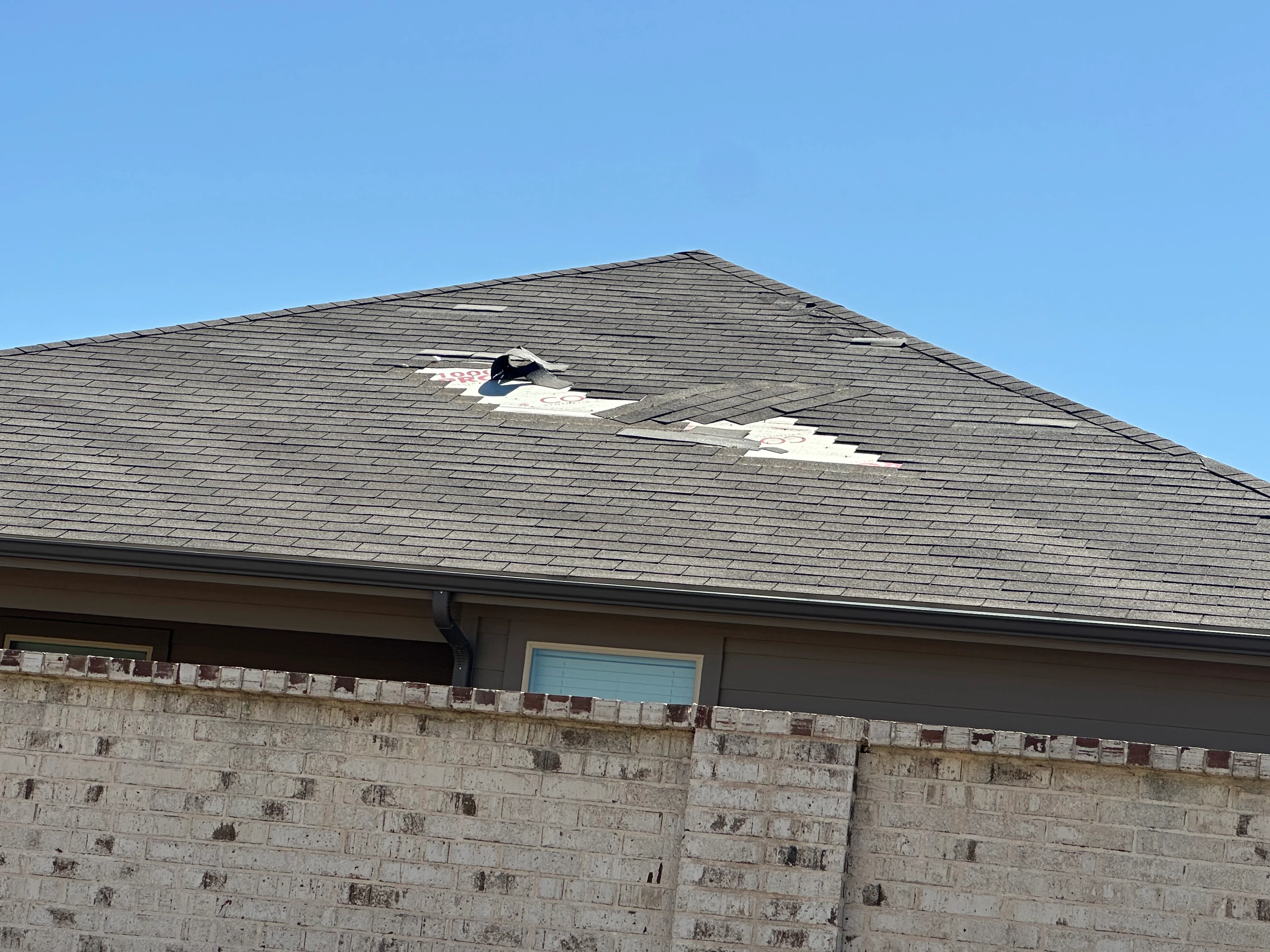Residential pitched roof with dark asphalt shingles showing storm damage and repair work