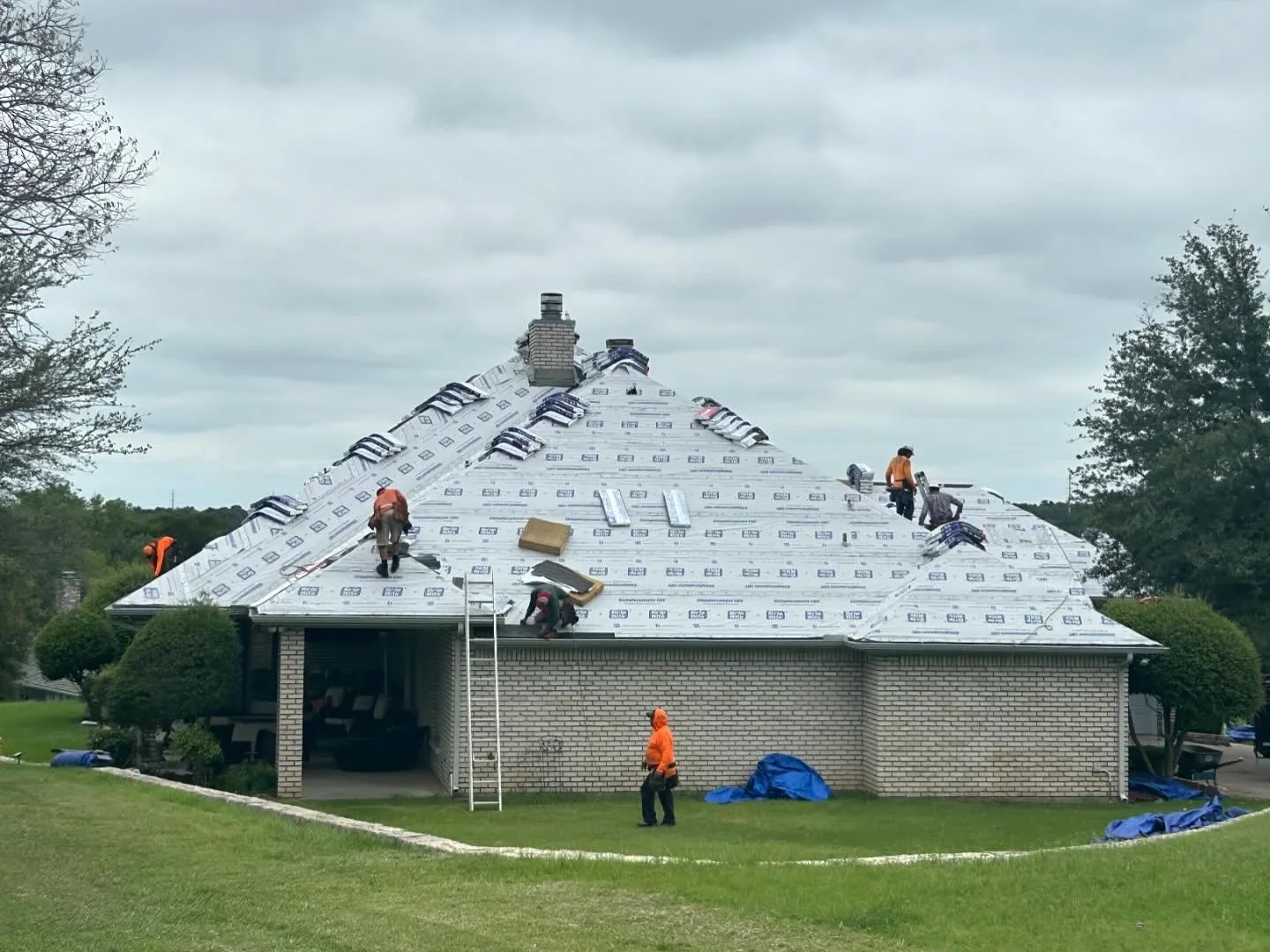 Roofers installing new underlayment and shingles on pitched residential roof with brick chimneys