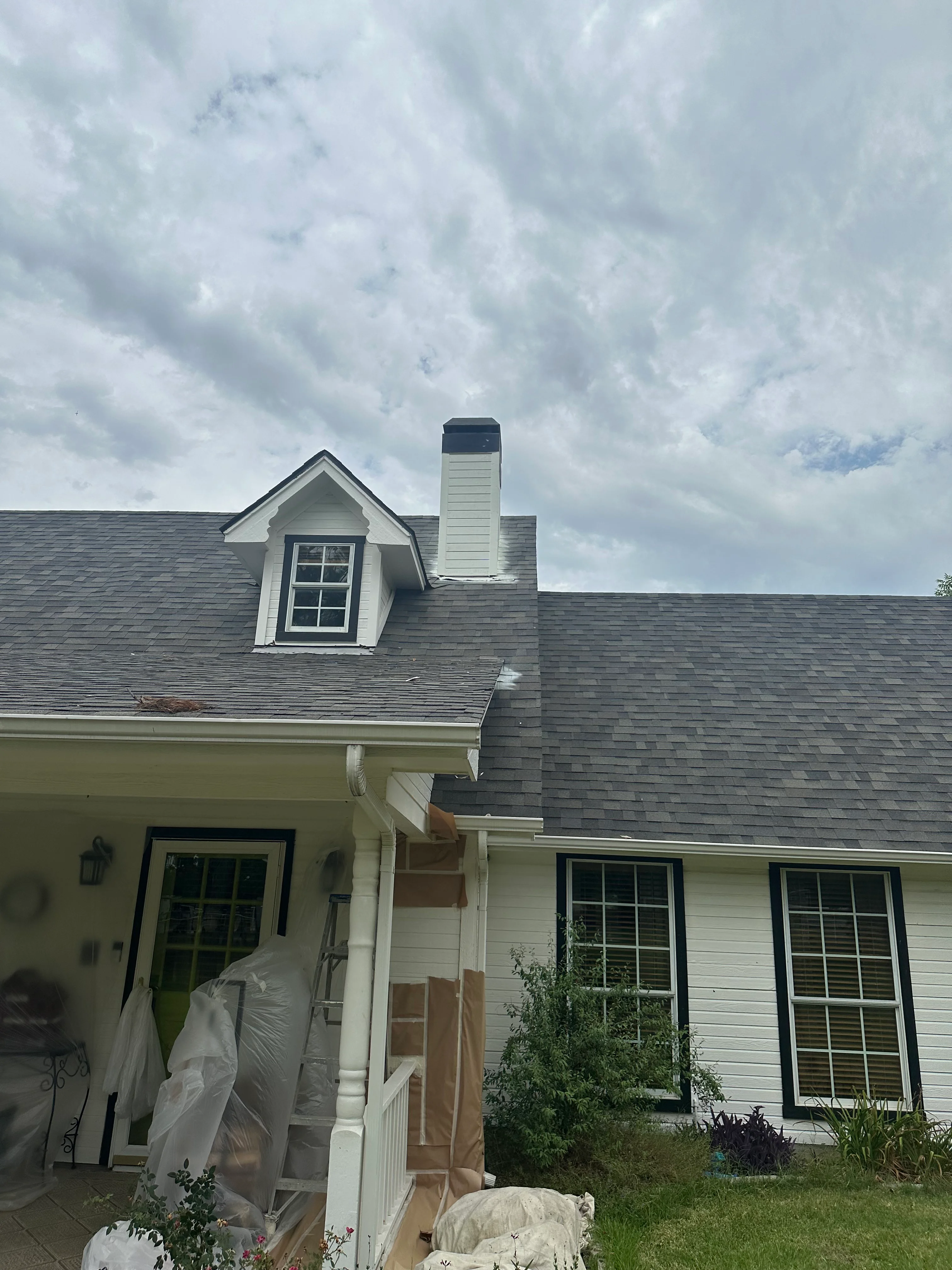 Residential roof with gray asphalt shingles, white dormer, and vinyl chimney flashing installation