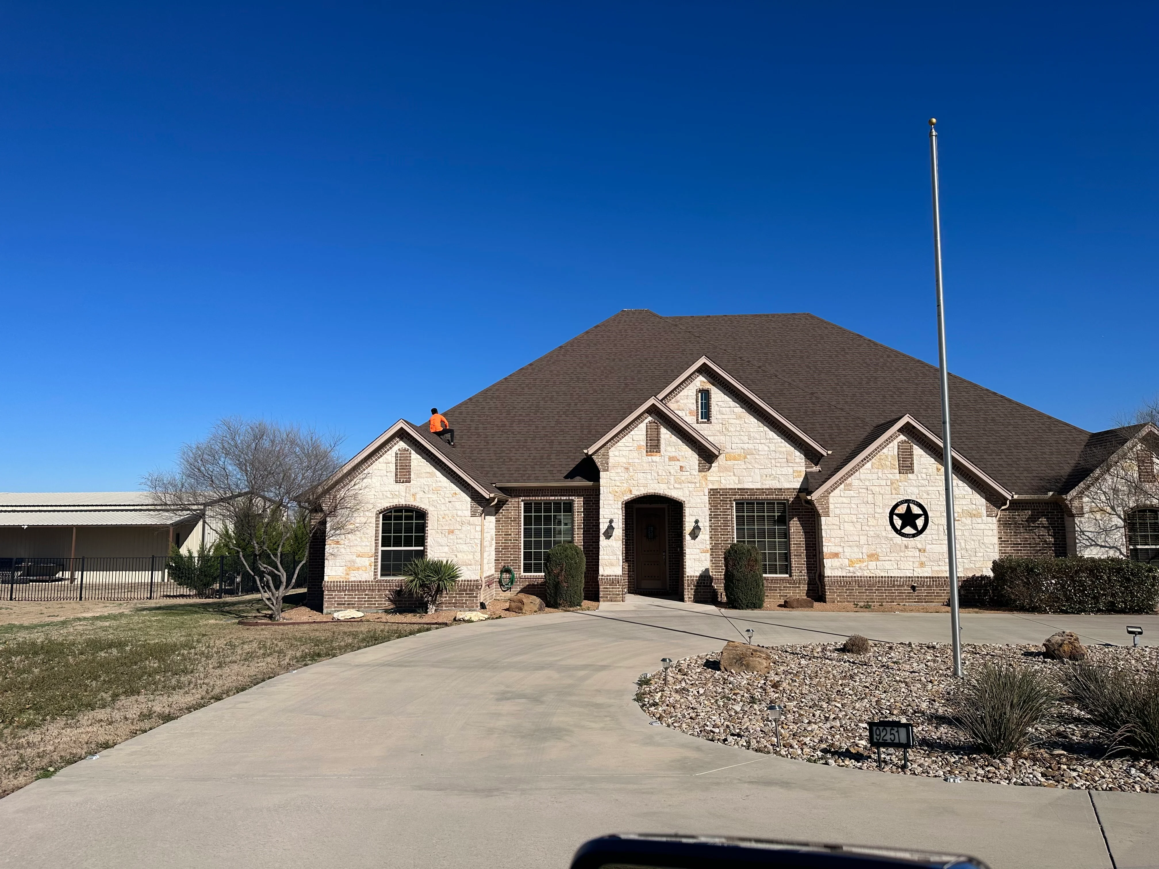 New charcoal gray asphalt shingle roof on two-story stone and brick residential home