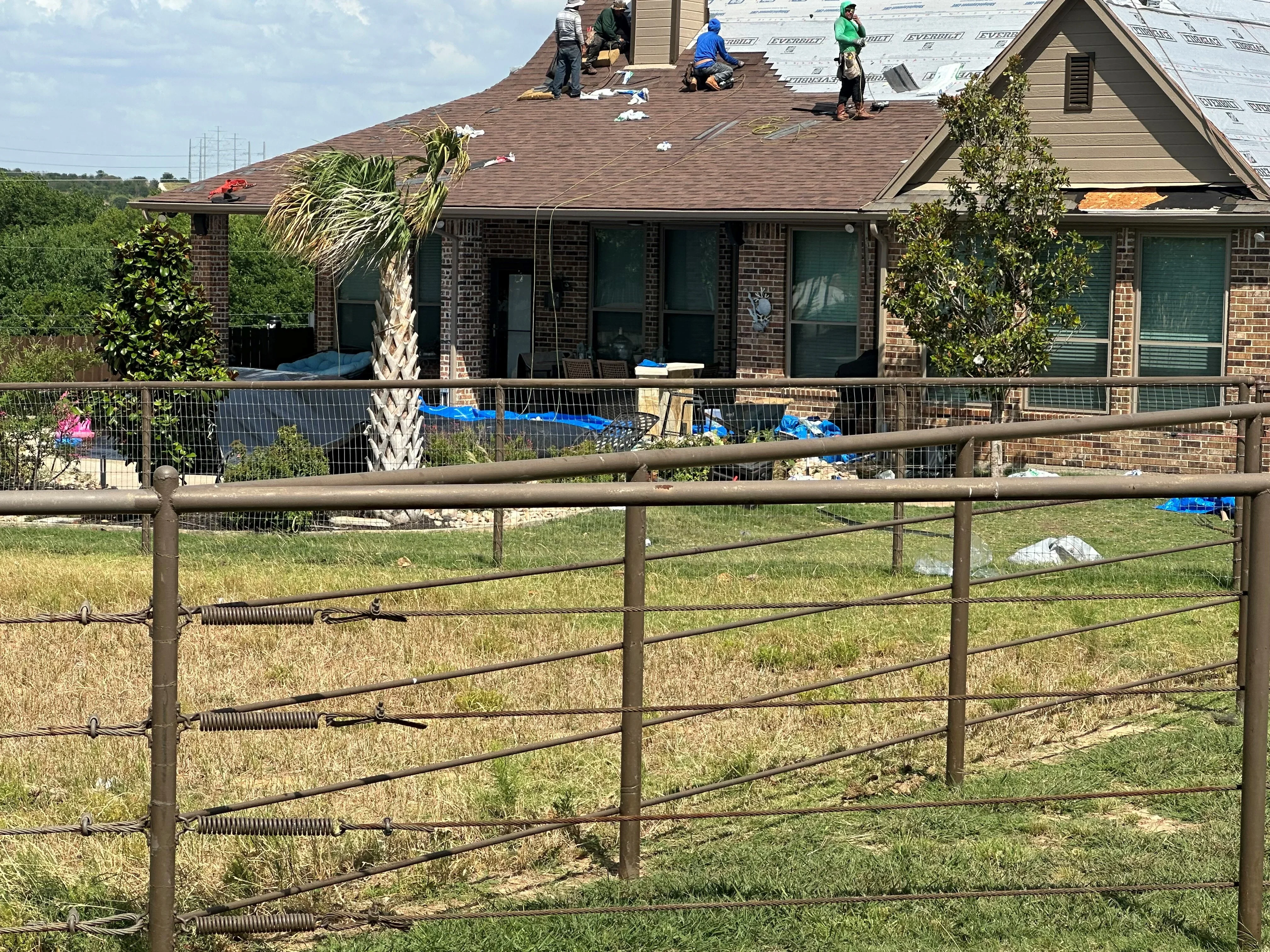 Roofers installing architectural shingles on brick home with multiple roof planes and protective underlayment