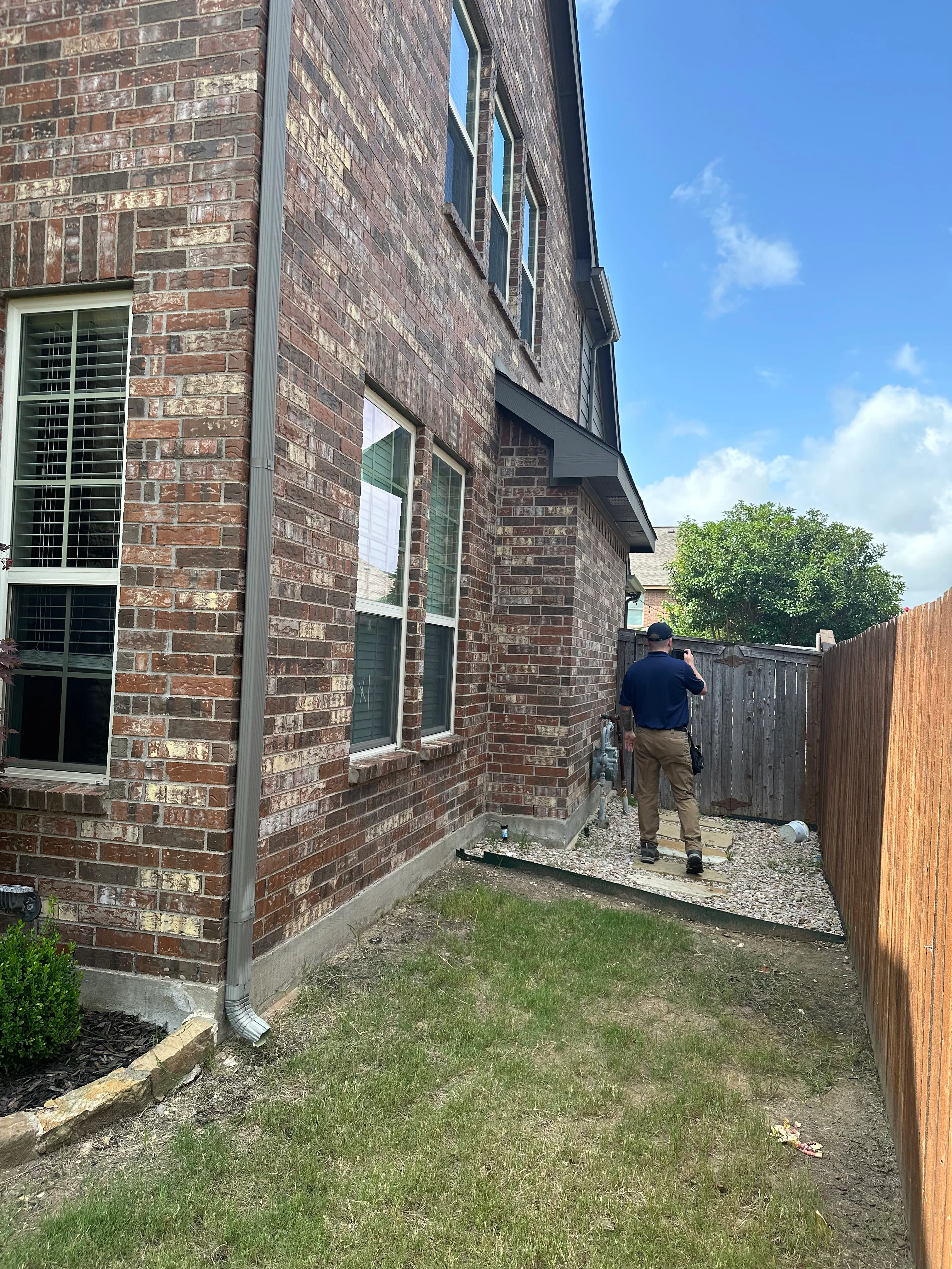 Brick home exterior with inspector evaluating roof line and gutters along side of house