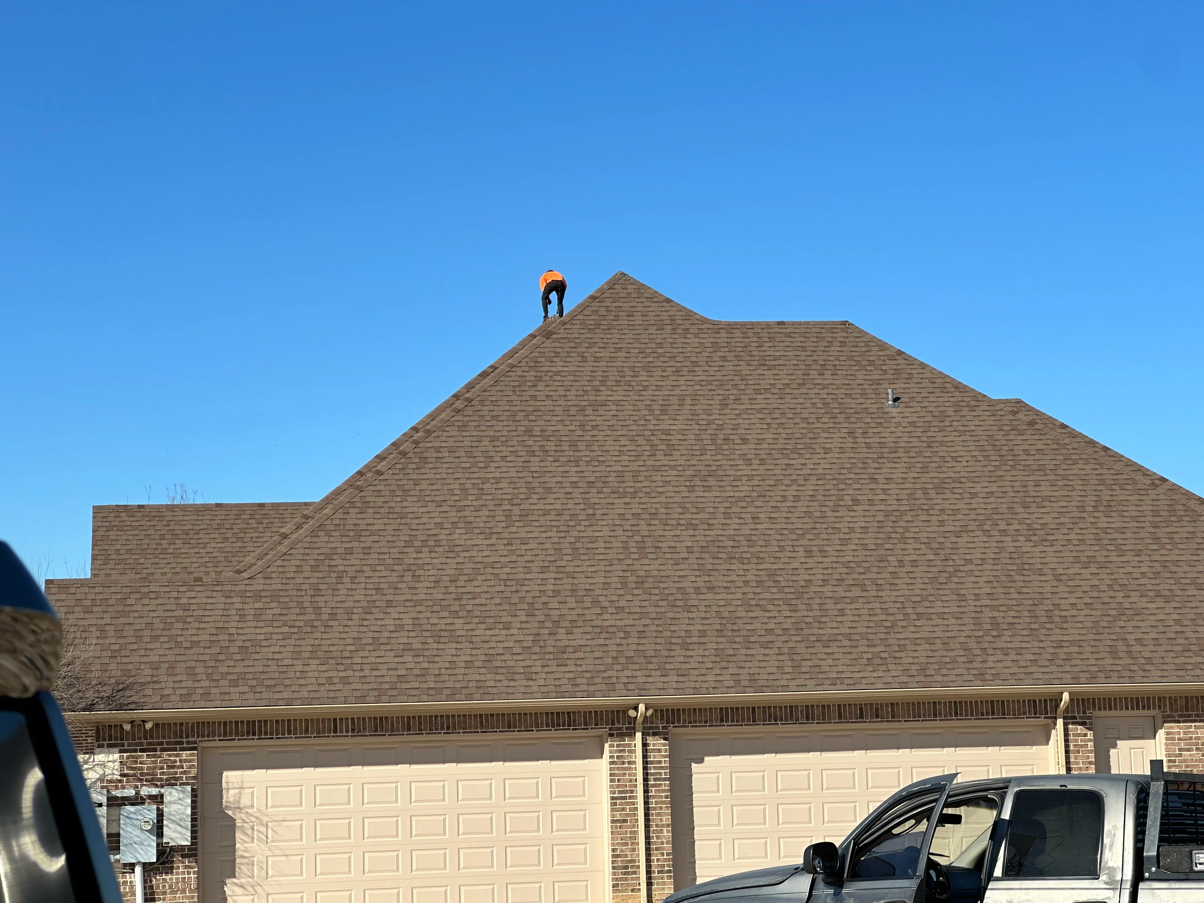 Worker installing gray asphalt shingles on residential gable roof with brick exterior