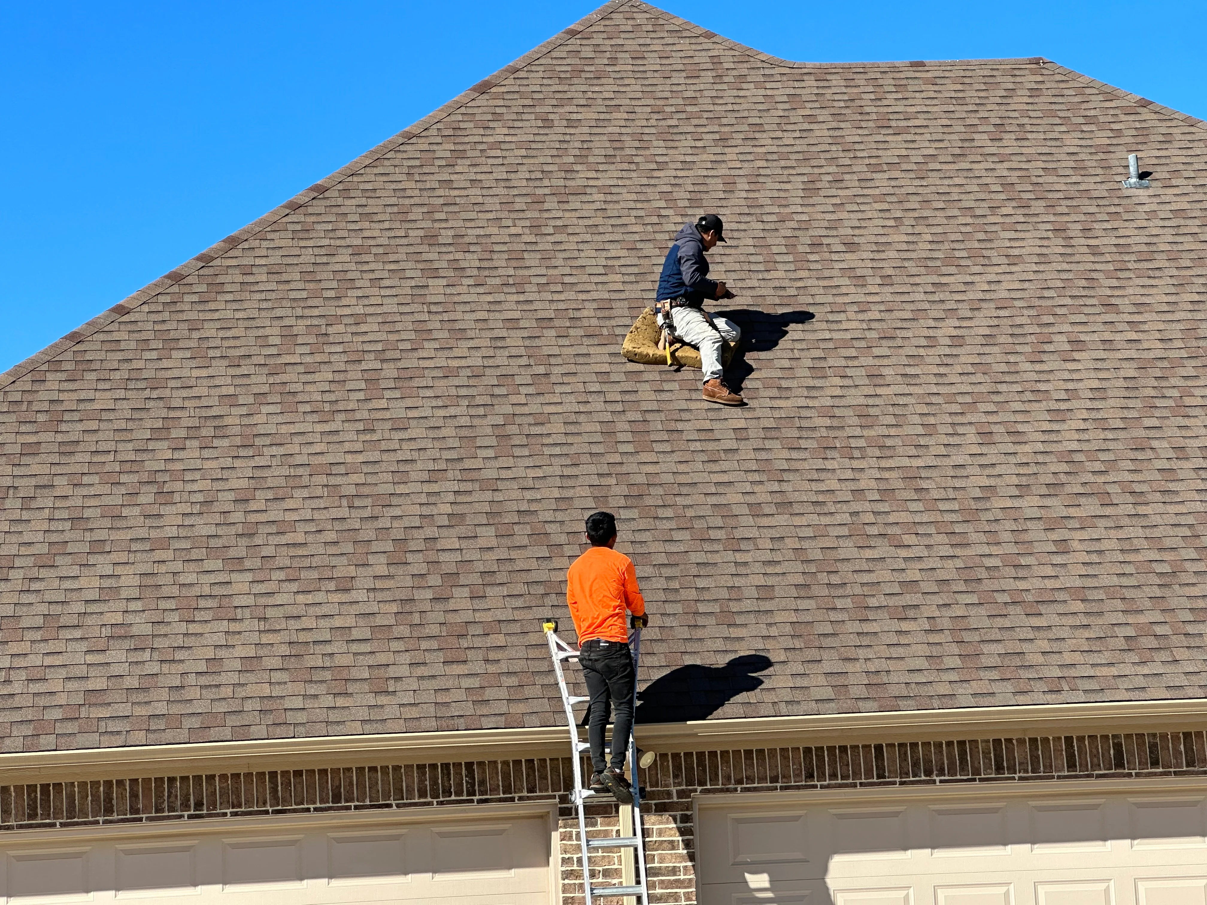 Roofers installing asphalt shingles on pitched residential roof with safety equipment