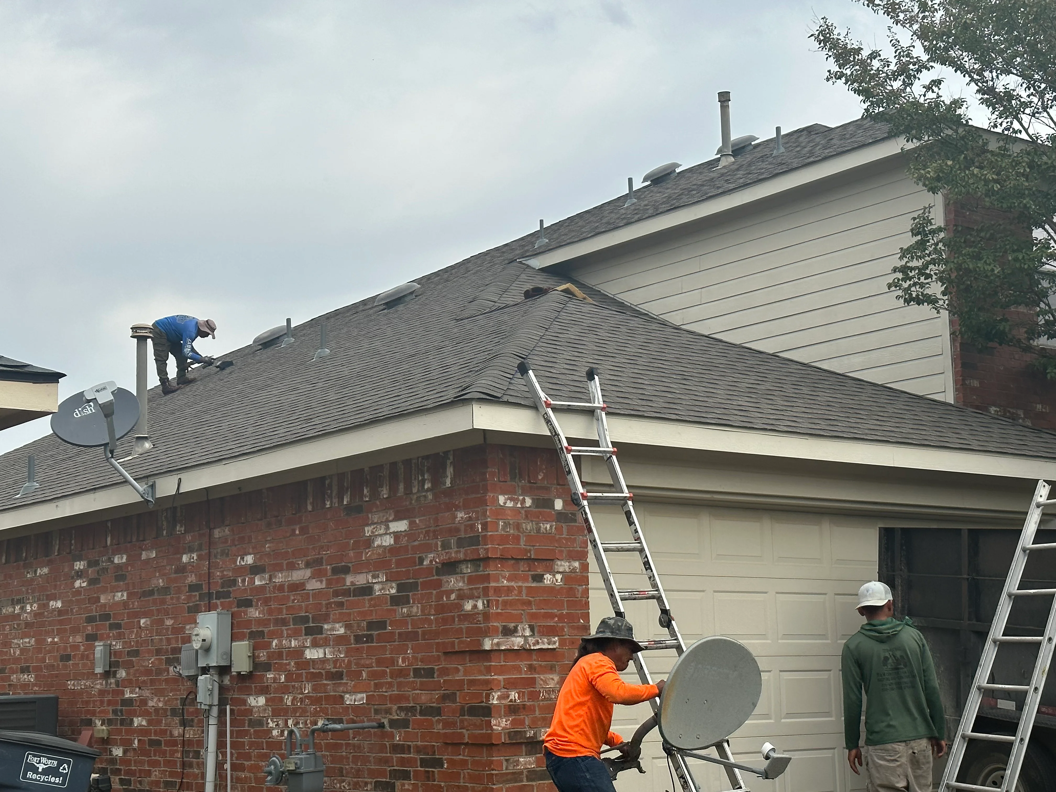 Roofing crew inspecting and working on asphalt shingle roof with ladders and safety equipment