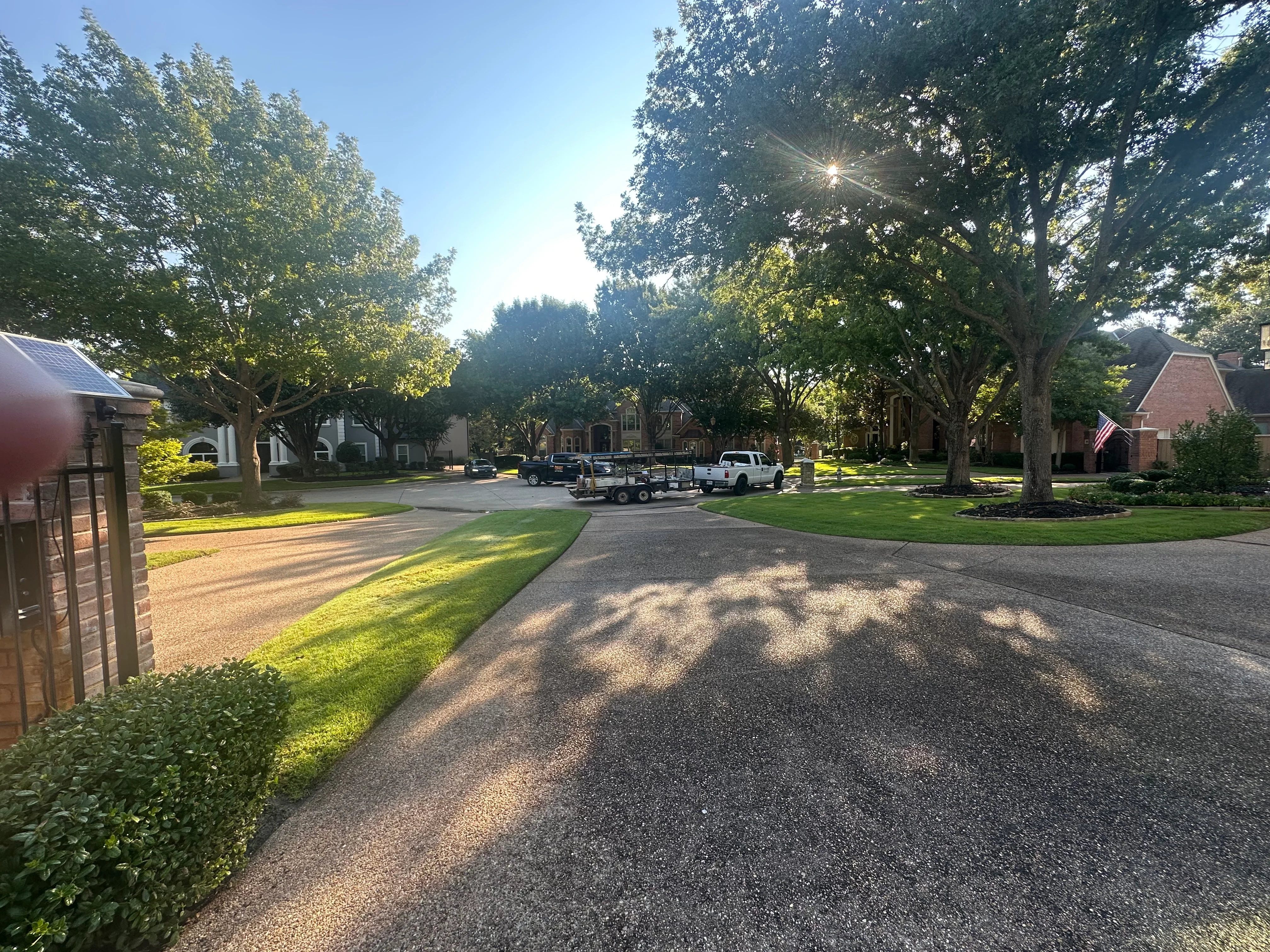 Residential street with brick homes, mature trees, and asphalt driveway