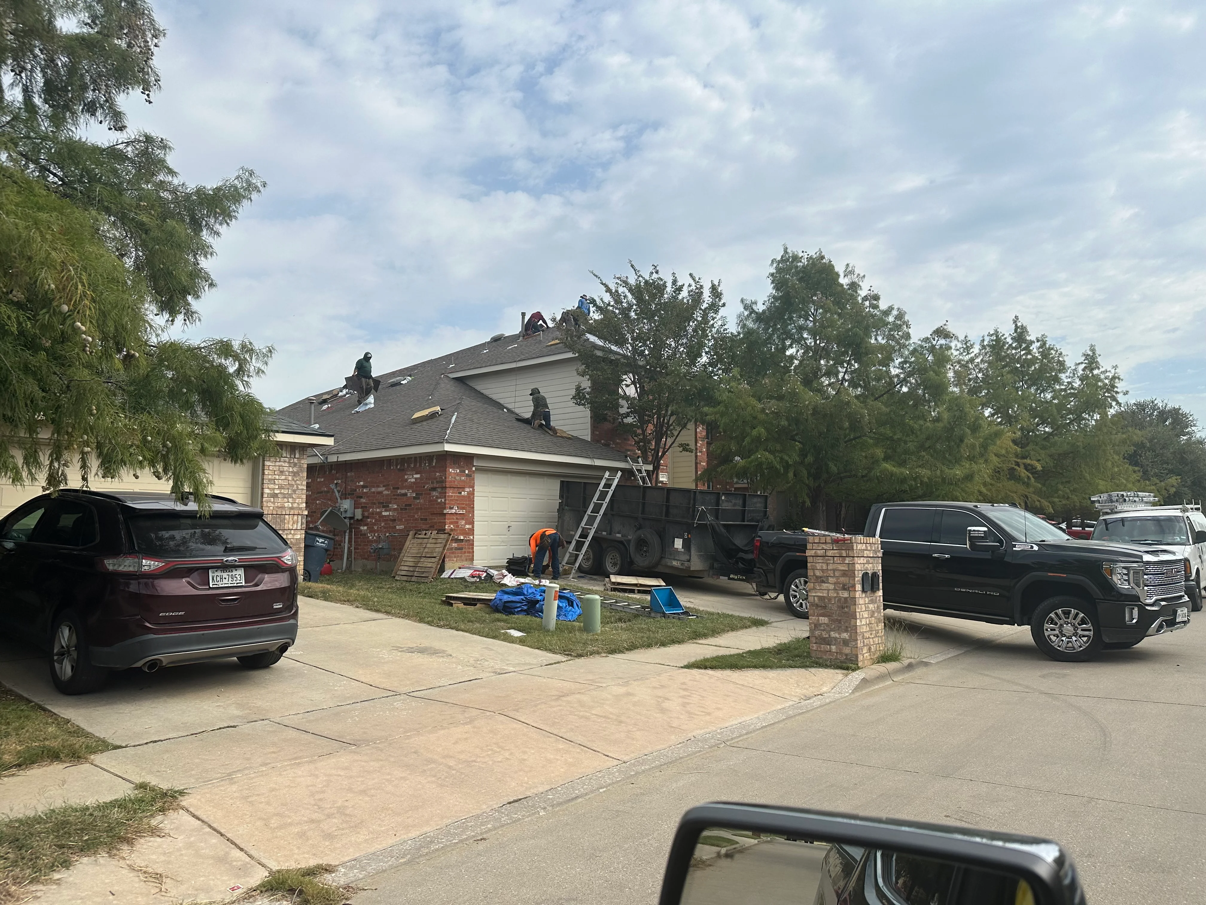 Roofers installing asphalt shingles on two-story home with brick and siding