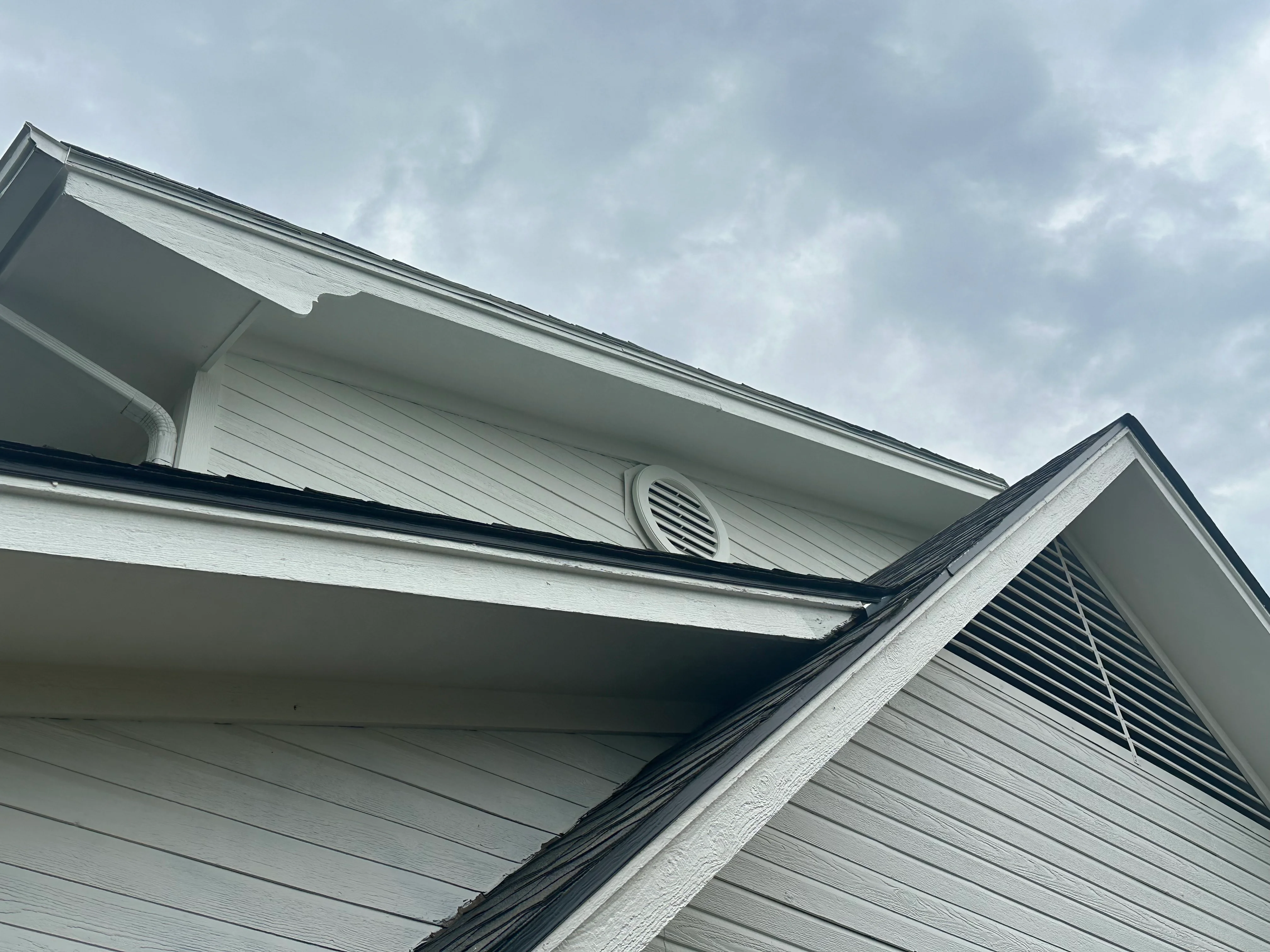 White vinyl soffit and fascia with dark trim, ventilation louvers, and gutter installation on residential roofline
