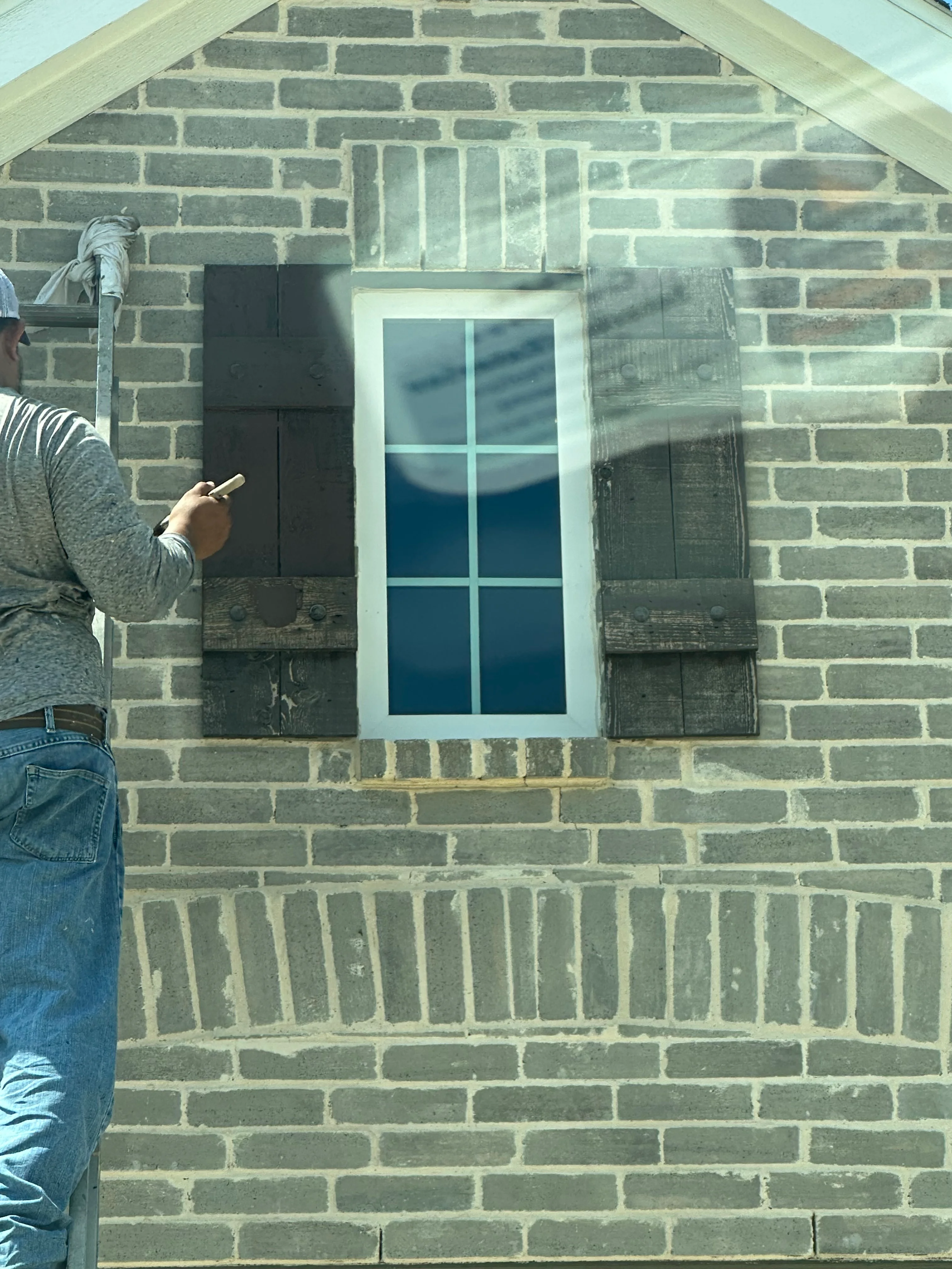 Black painted shutters and white trim on brick exterior wall with 6-pane window