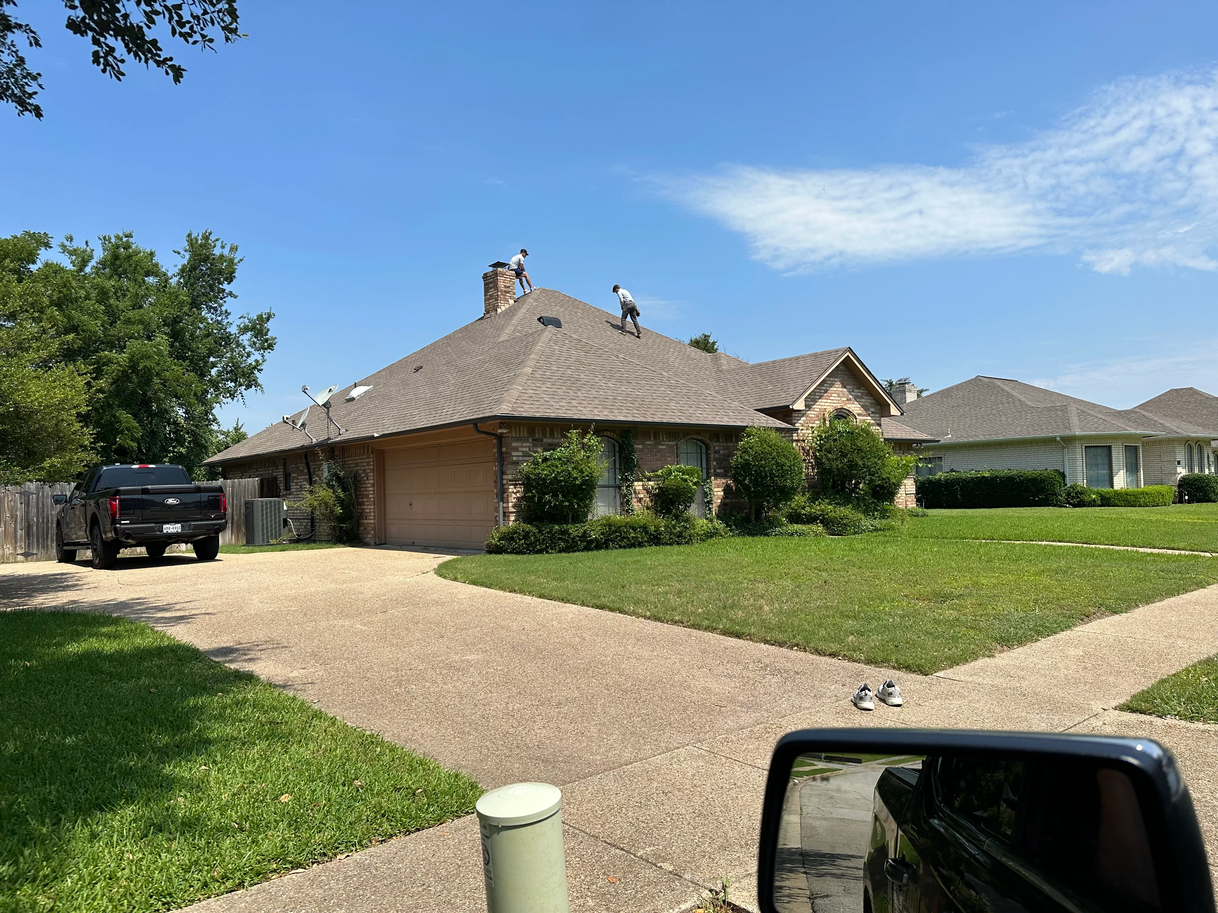 Gray architectural shingles installed on residential roof with brick chimney and stone exterior
