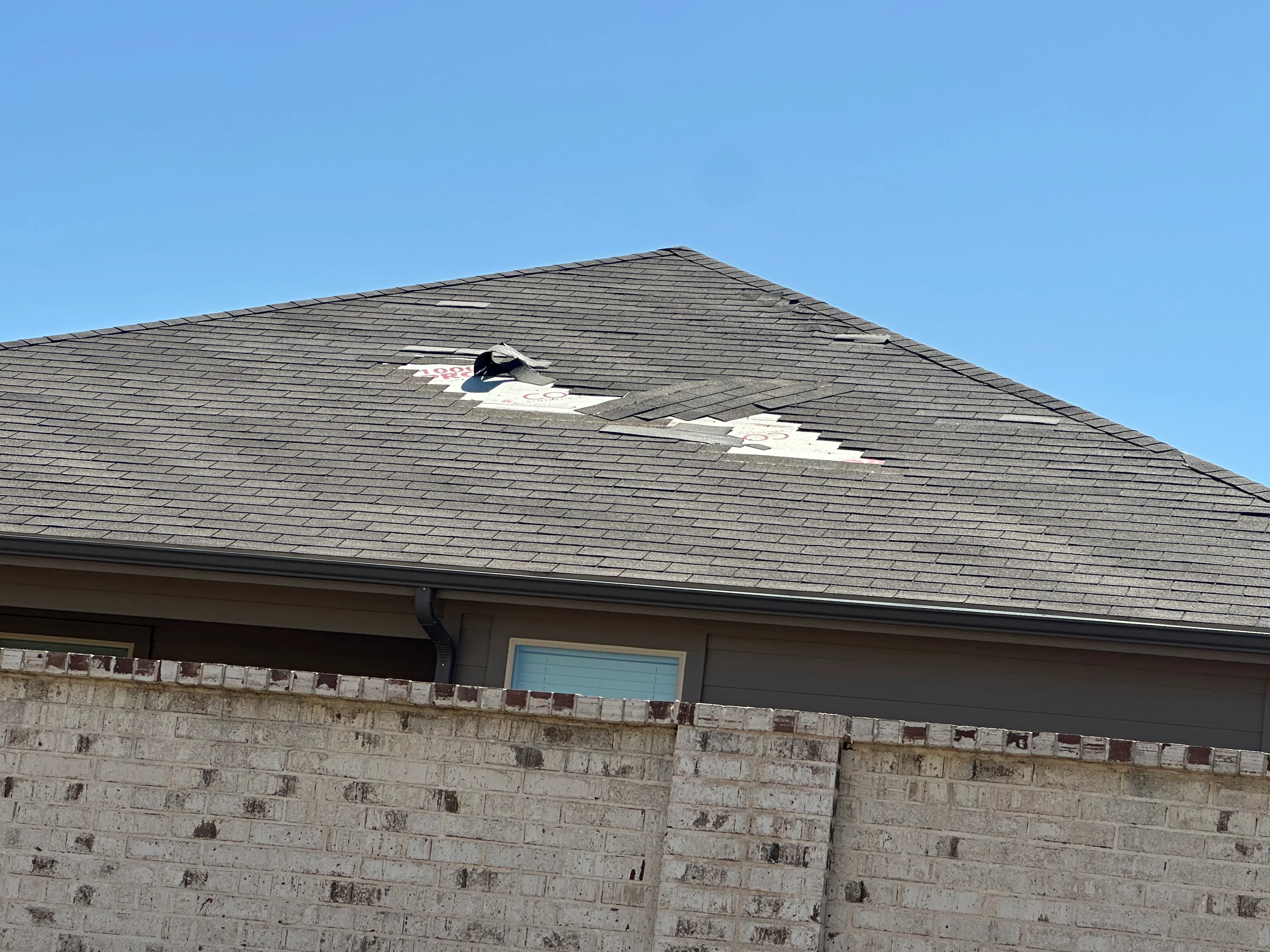 Asphalt shingle roof with storm damage and exposed underlayment requiring repair