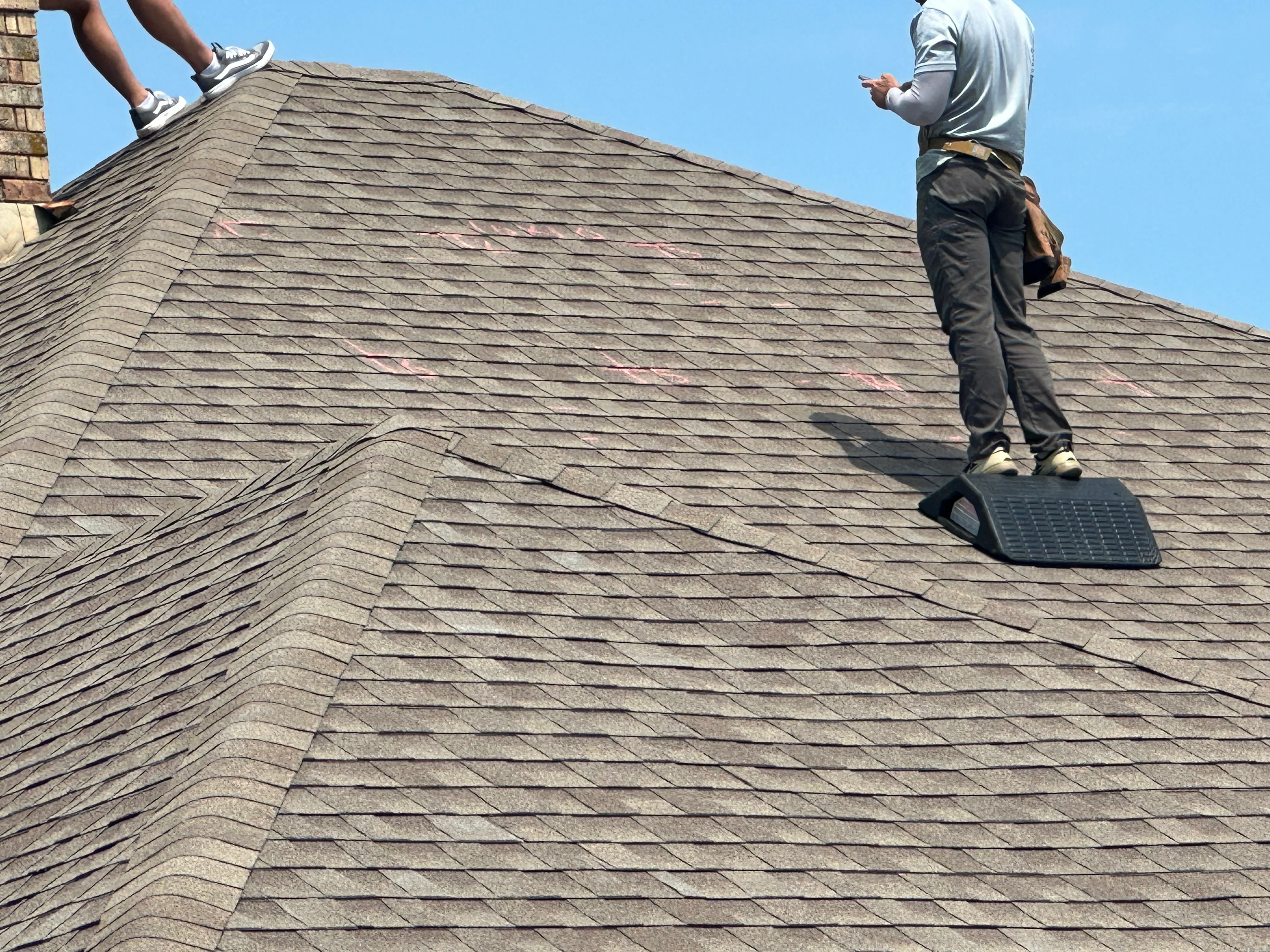 Roofers inspecting gray asphalt shingle roof with valleys and brick chimney