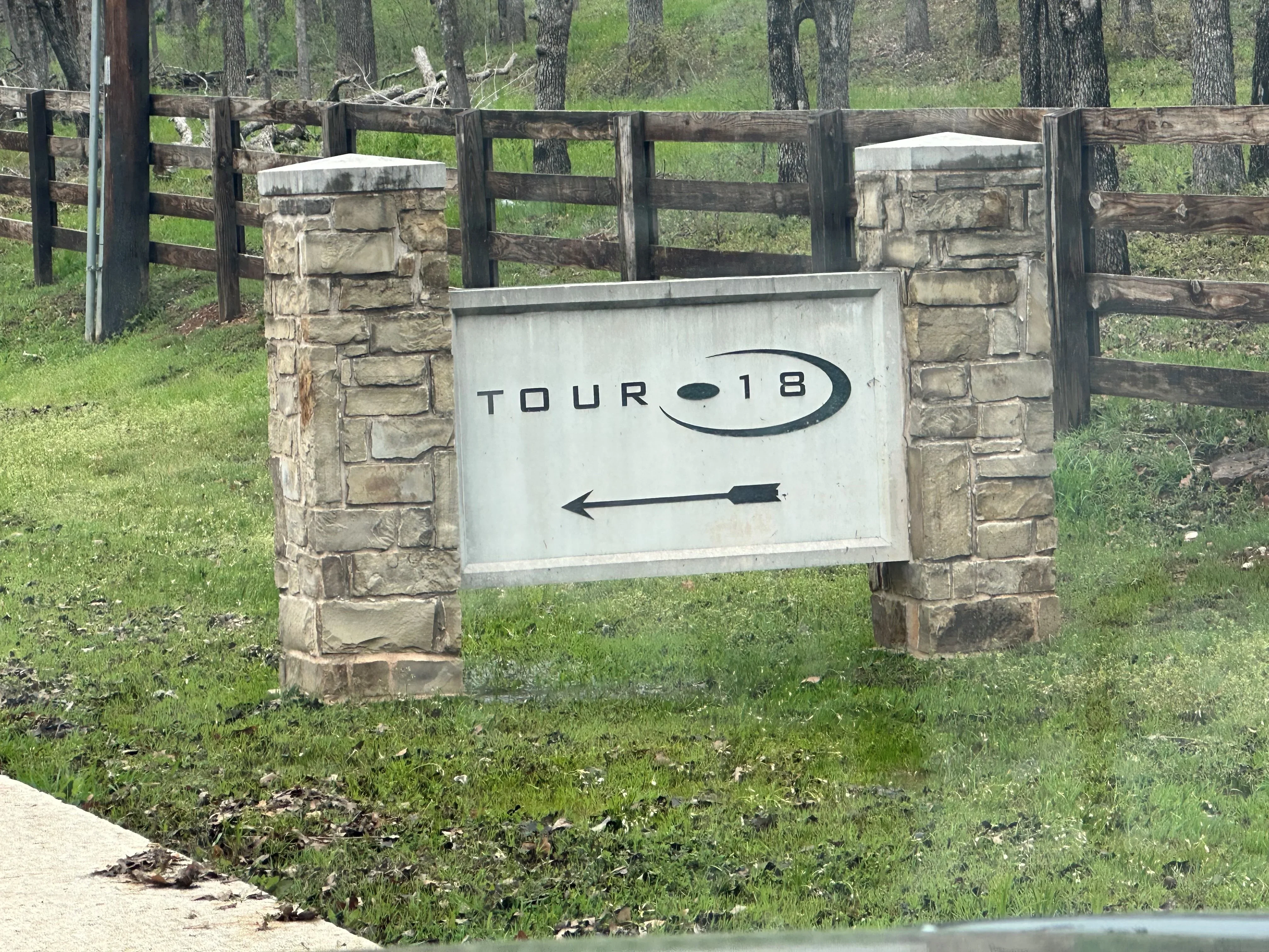 White metal sign with black text mounted on stone pillars between wooden ranch fencing