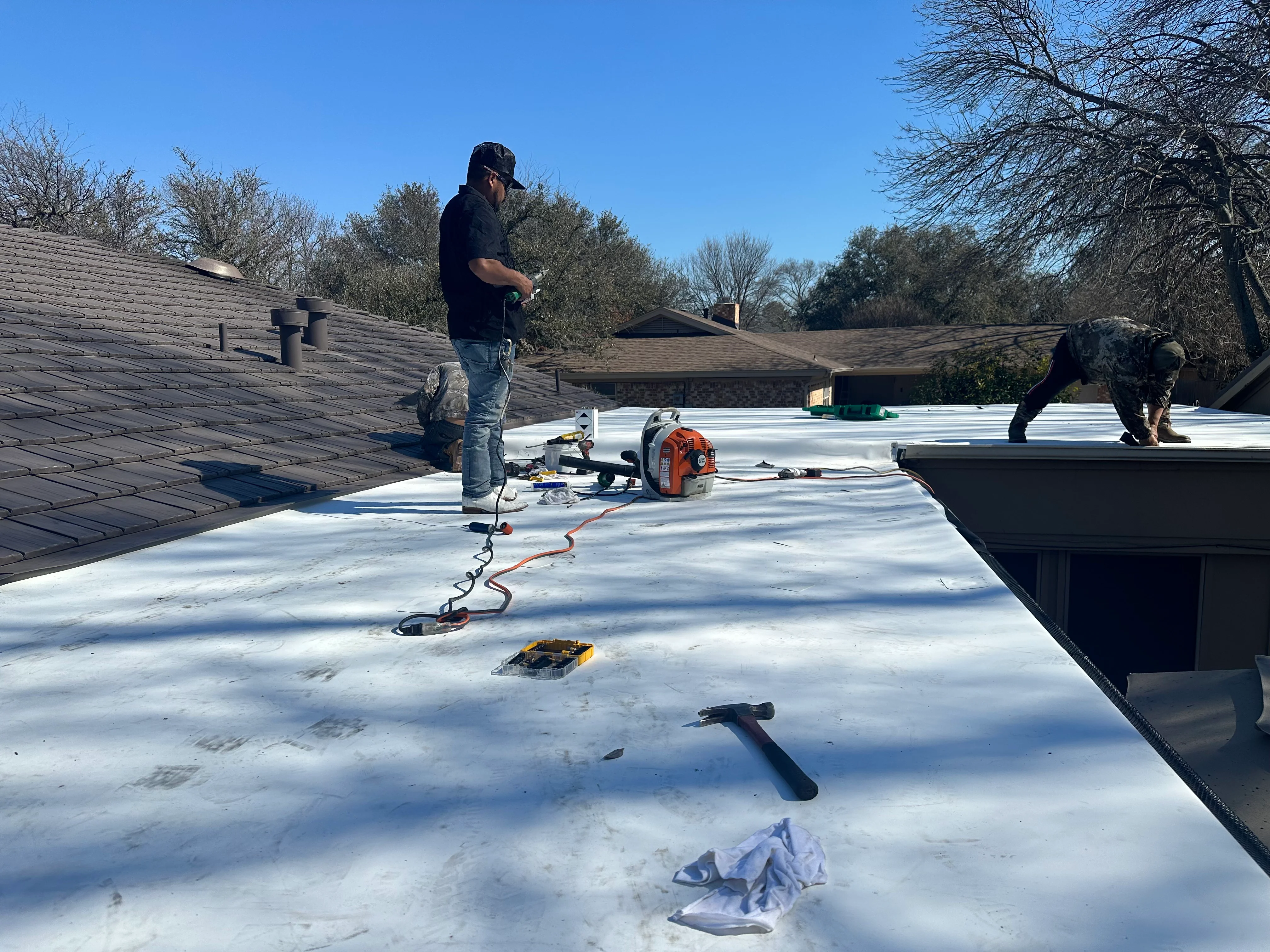 Workers installing white TPO membrane on flat roof with sealing equipment and tools