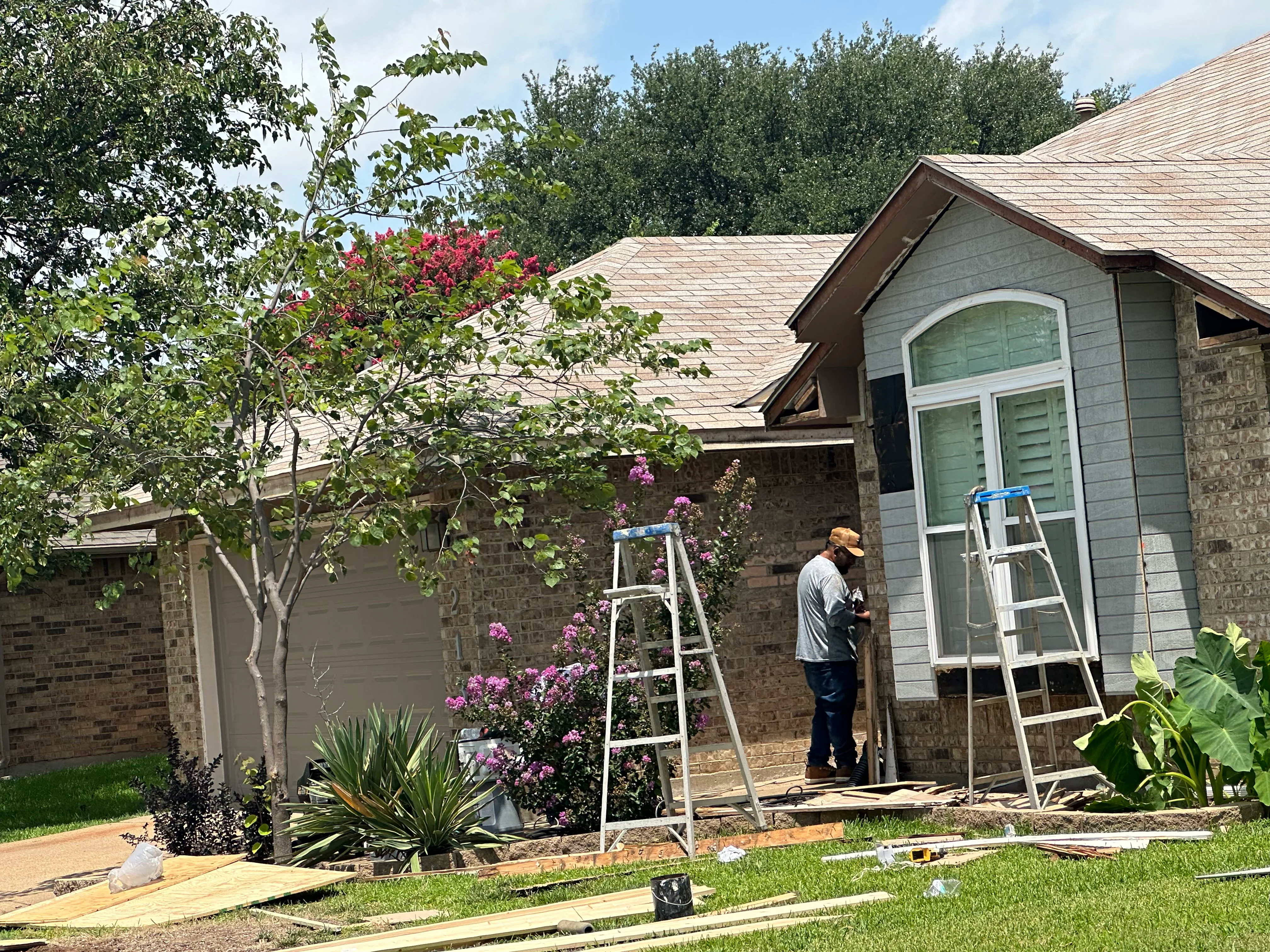 Roofer installing architectural shingles on brick home with multiple roof planes