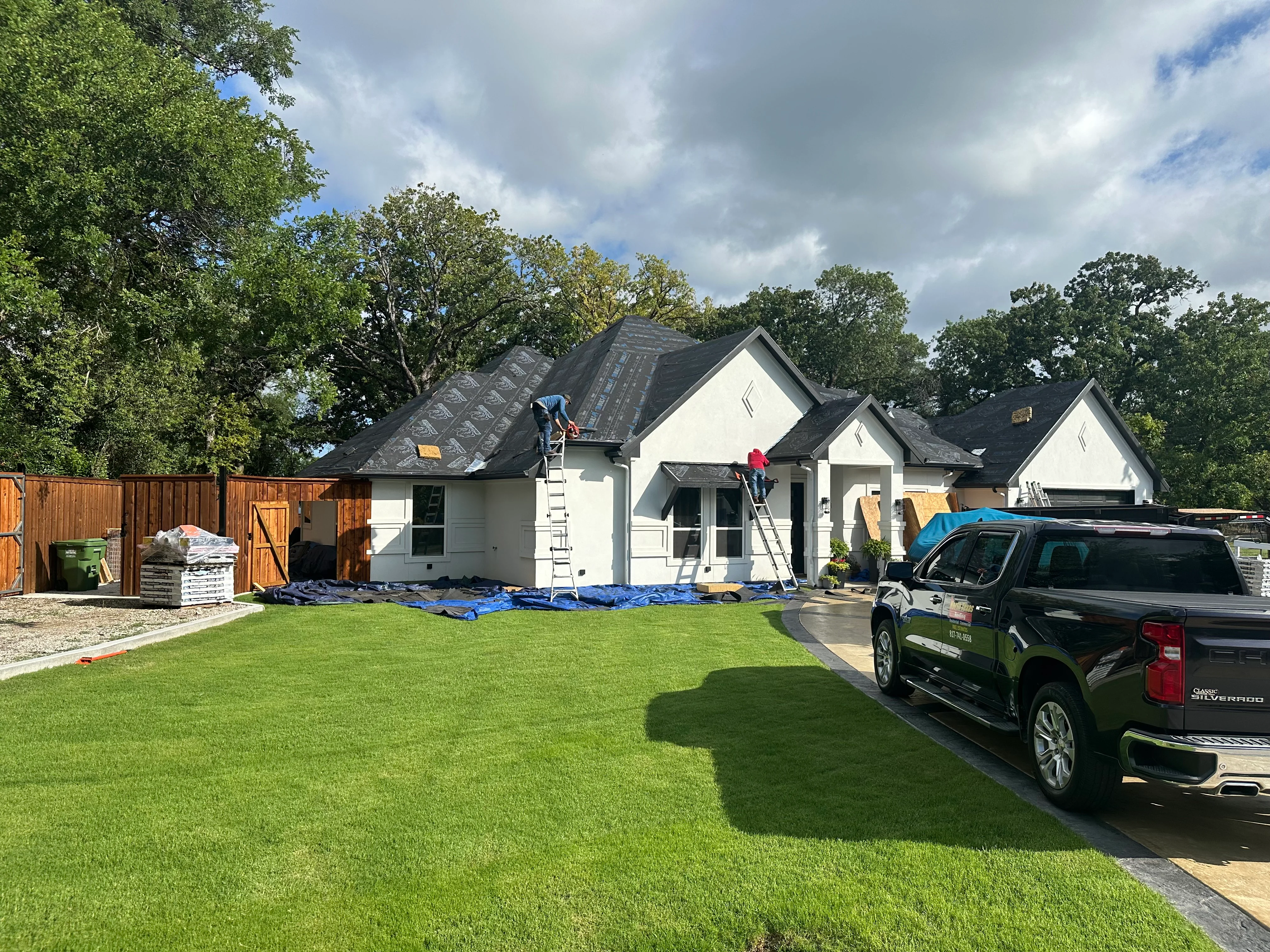 Roofers installing dark gray architectural shingles on white home with multiple roof peaks