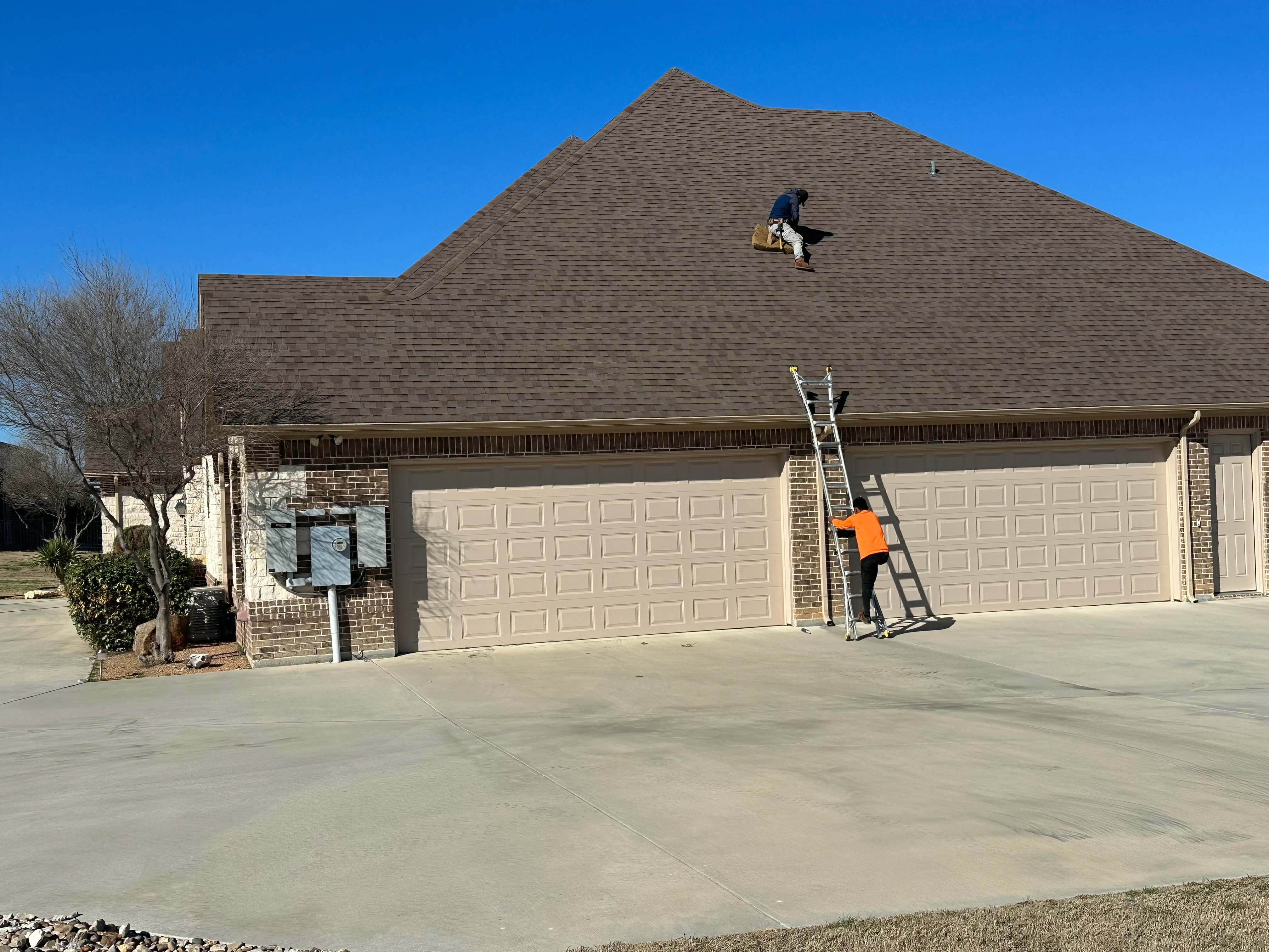 Roofers installing gray architectural shingles on pitched residential roof with ladder access