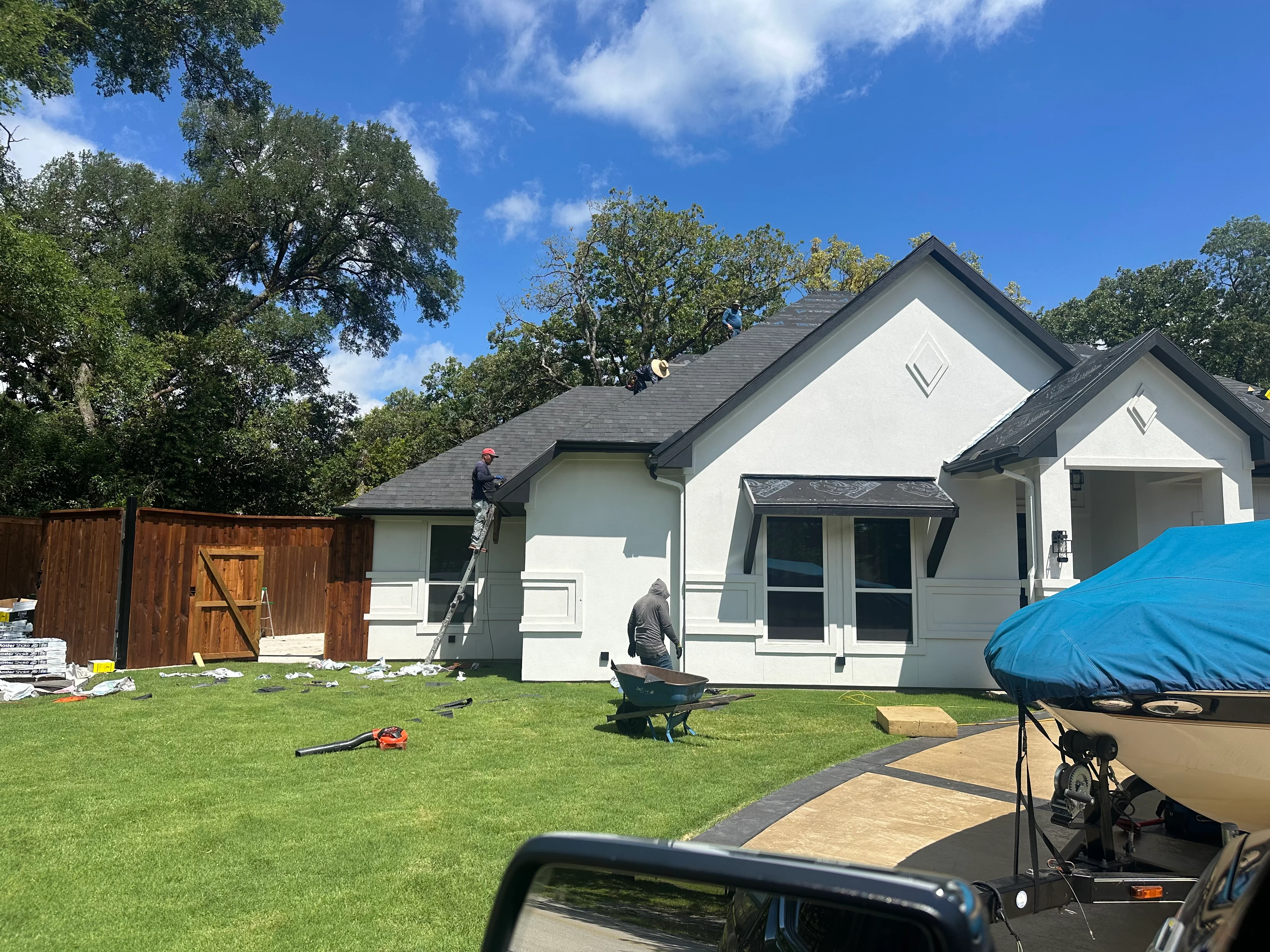 Roofers installing charcoal gray architectural shingles on residential home with white siding