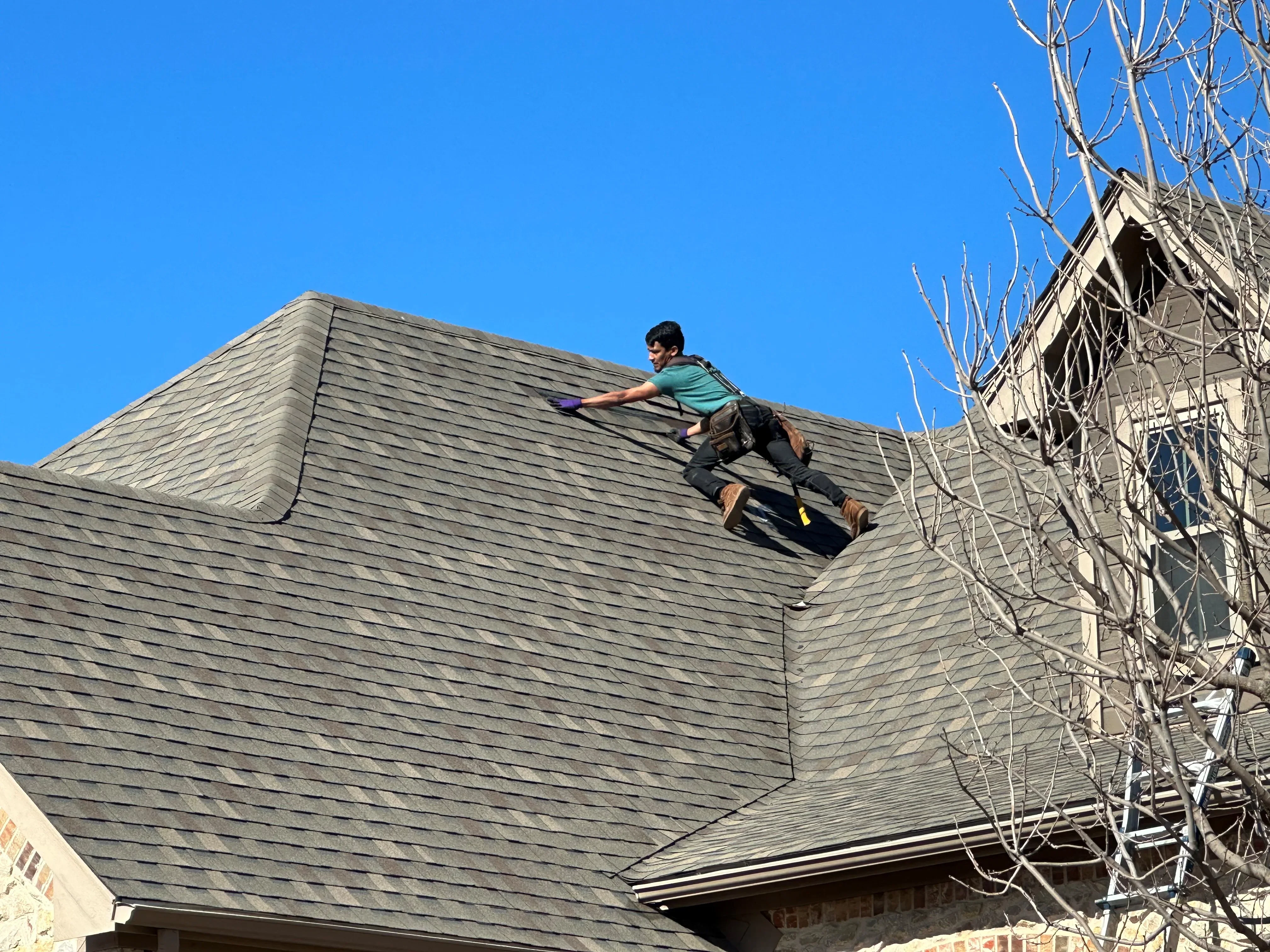 Worker installing gray-green architectural shingles on pitched residential roof with multiple angles