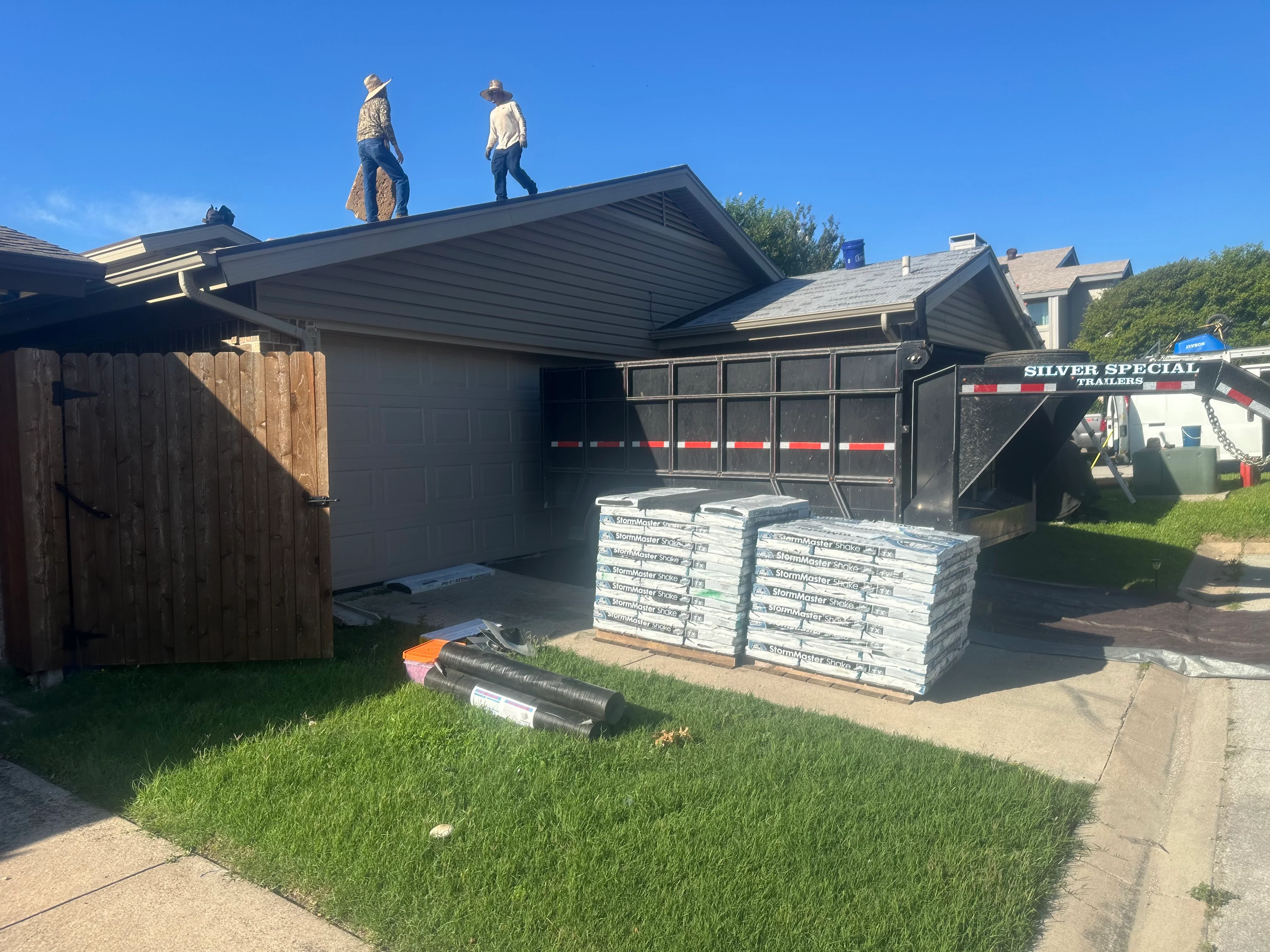 Residential roof replacement with new shingles, staged materials, and workers on roof