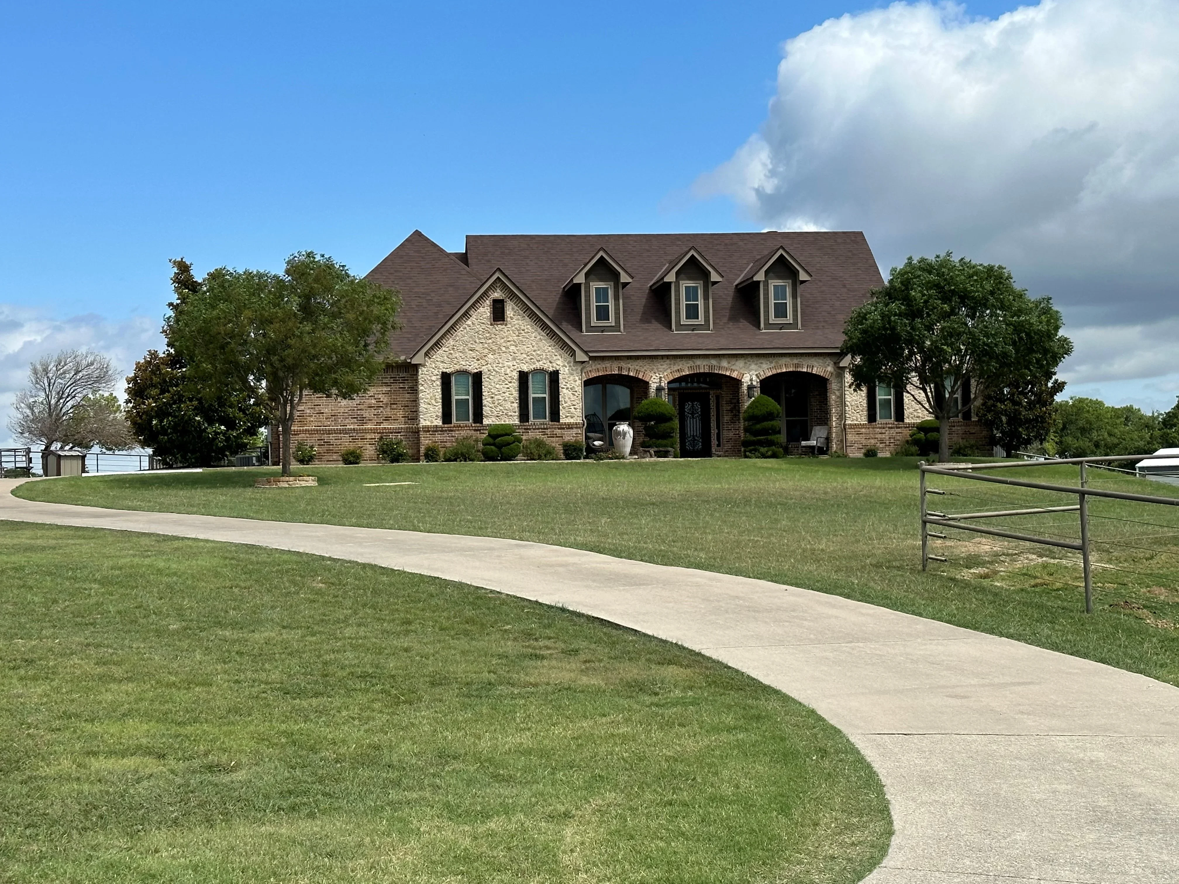 Dark brown architectural shingles on pitched roof with three dormers, brick and stone home