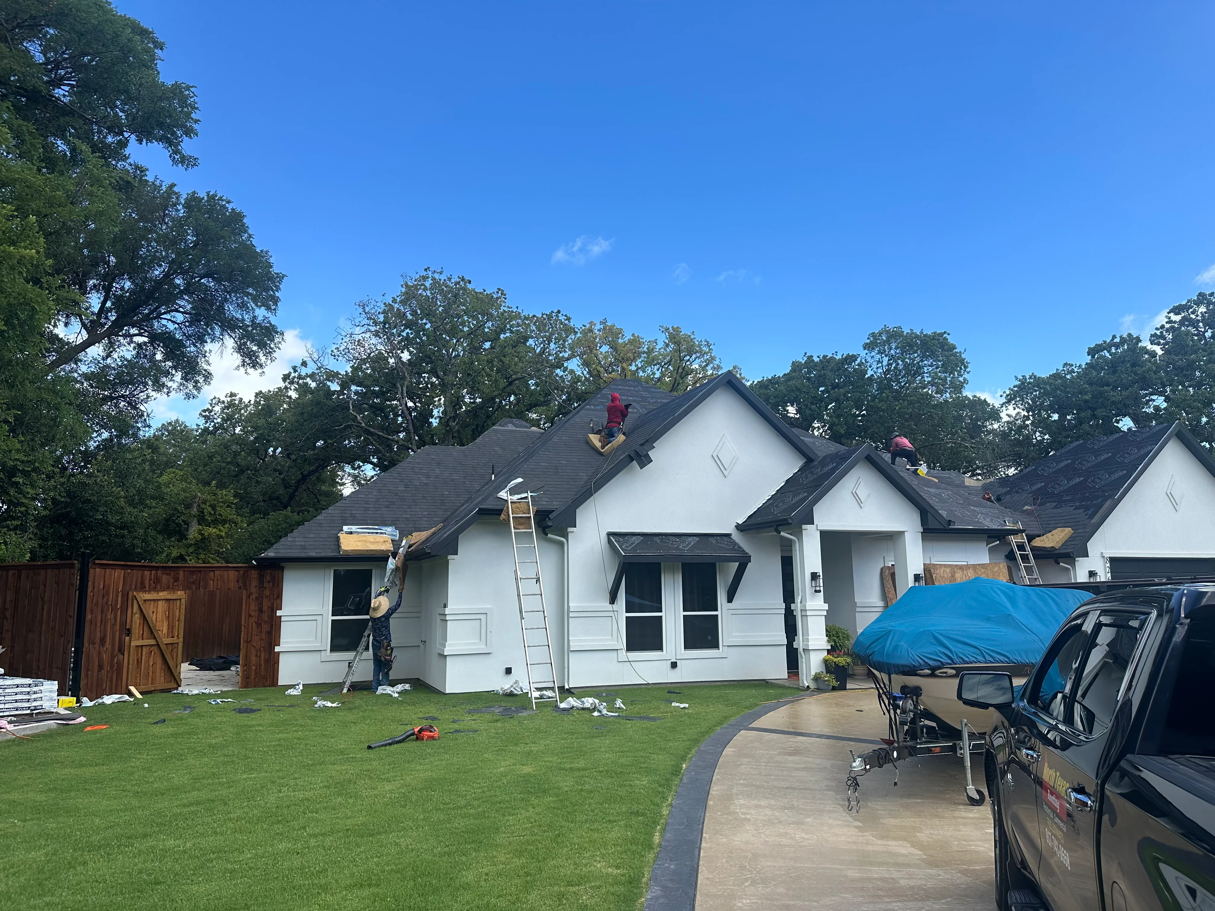 Residential roof replacement with dark shingles on white home, workers on pitched roof with ladders and materials