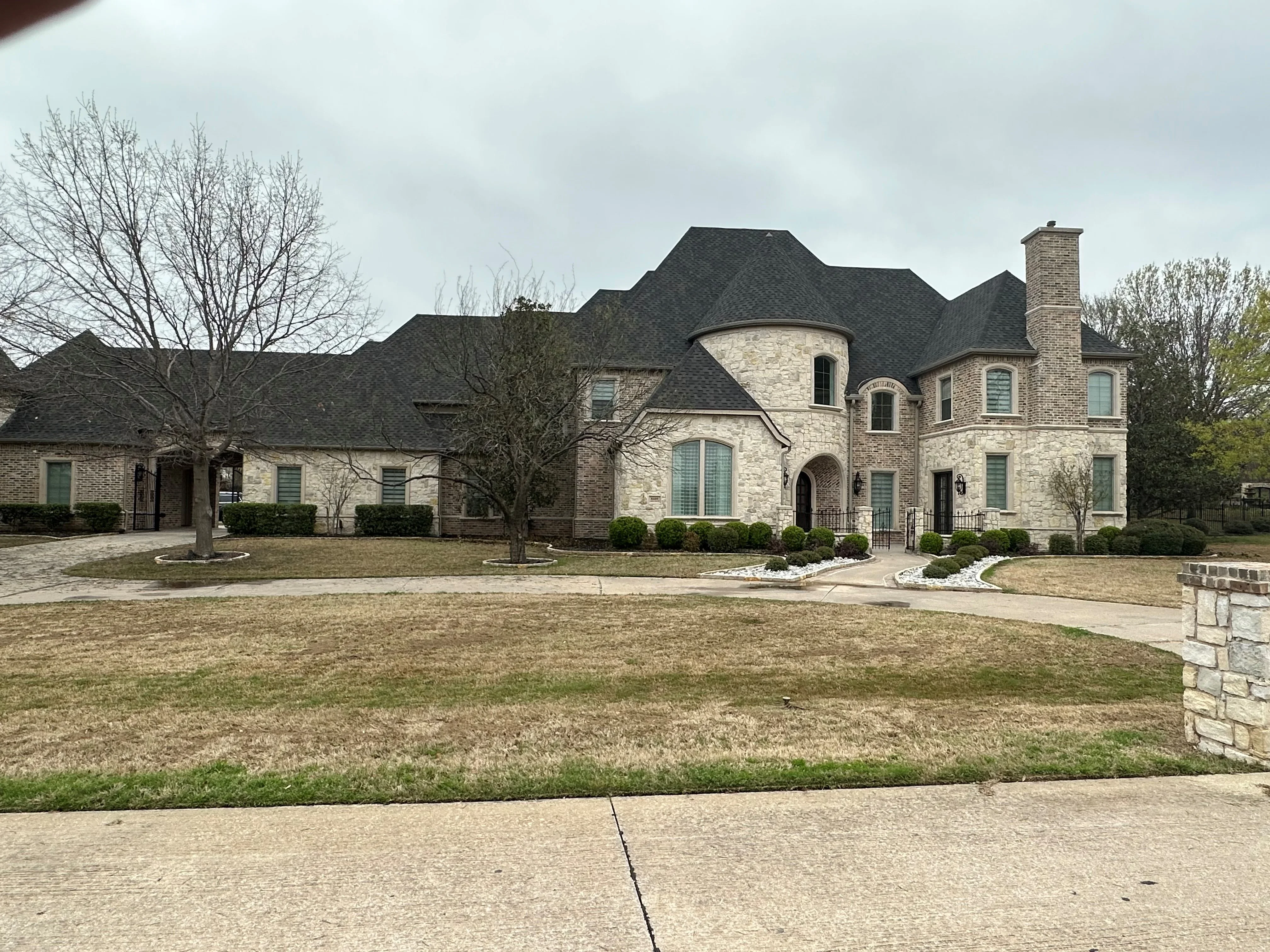 Two-story brick home with dark asphalt shingle roof, multiple peaks and turrets