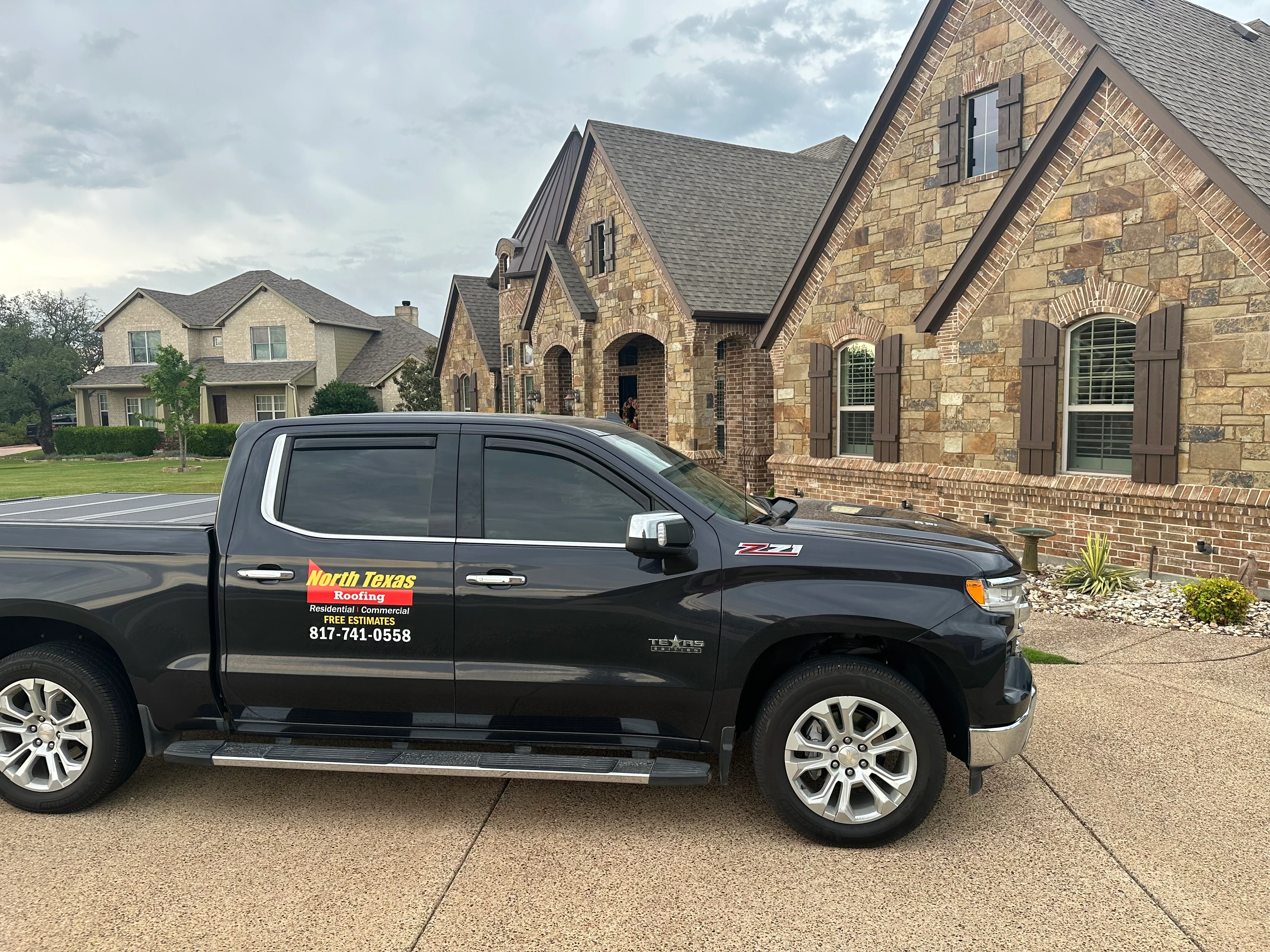 Gray asphalt shingles on multi-peak residential roof with stone and brick exterior