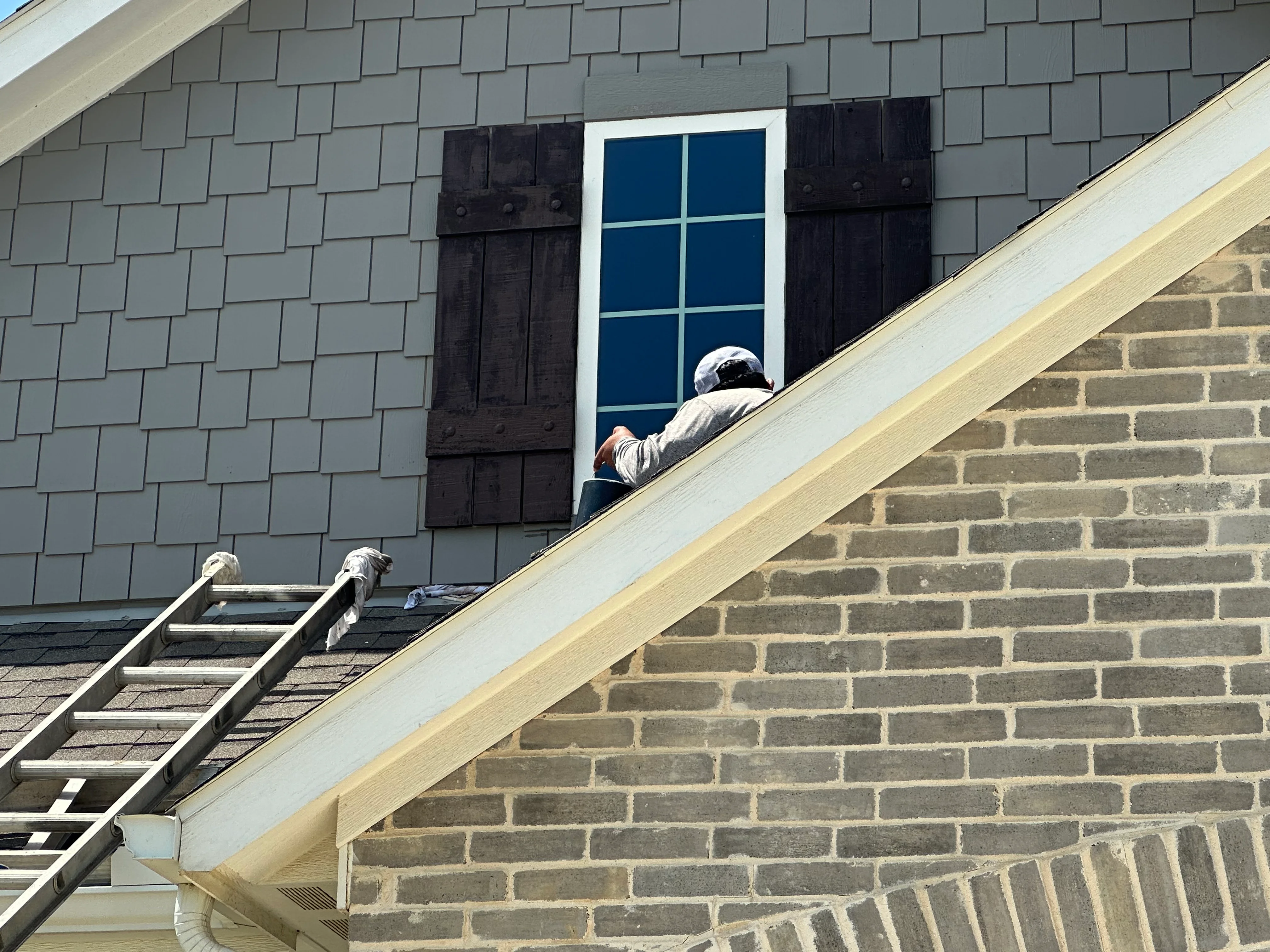 Worker installing new window in gable with gray composite shingles and white trim