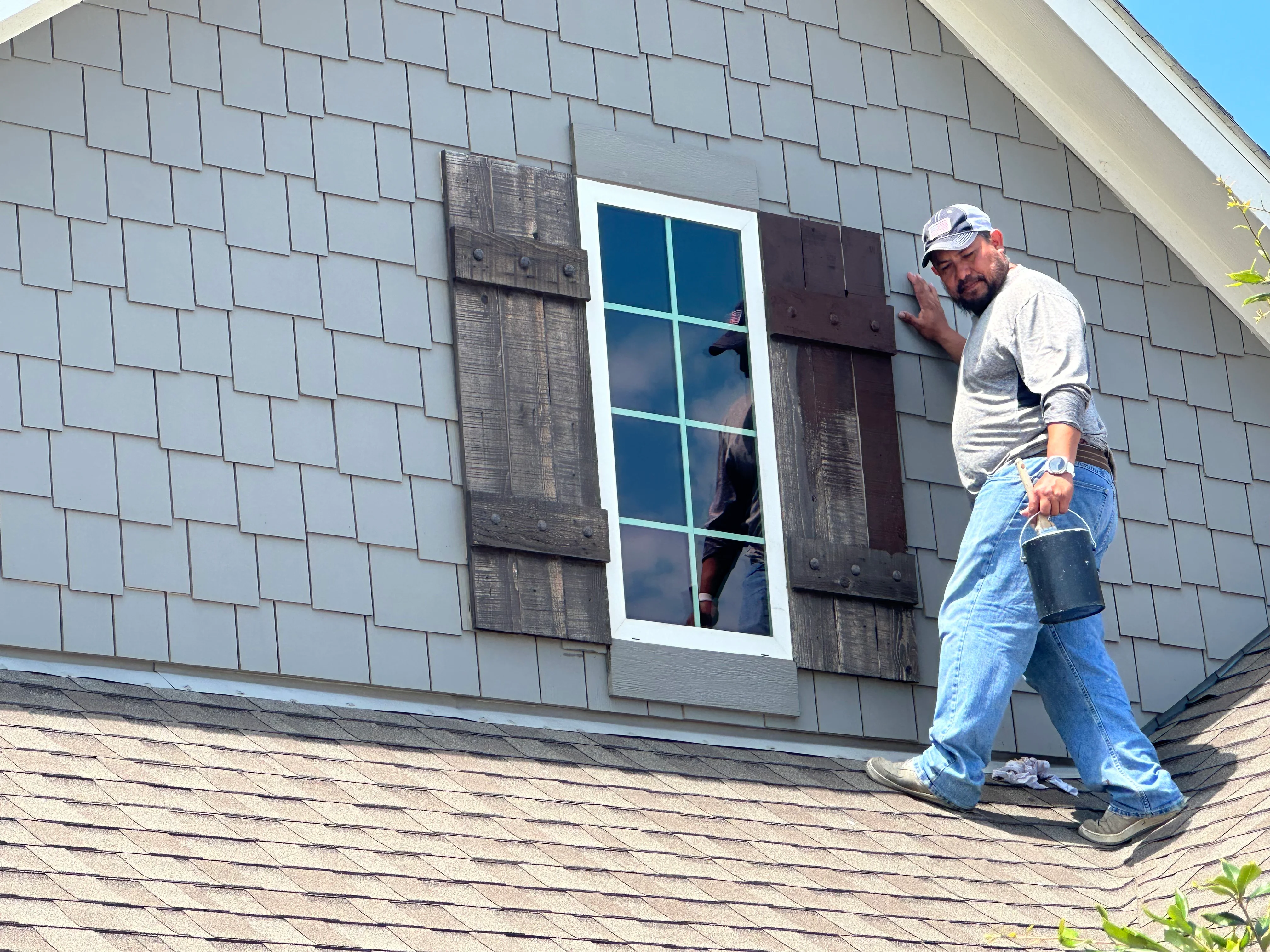 Gray composite shingles with dark wood shutters and white-trimmed window installation on pitched roof