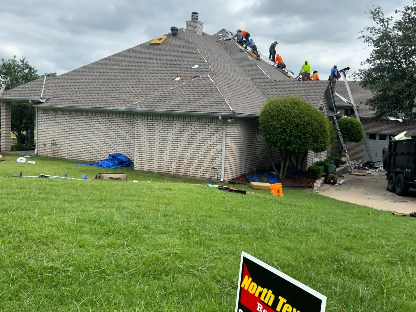 Roofers installing gray architectural shingles on multi-plane residential roof with brick chimney