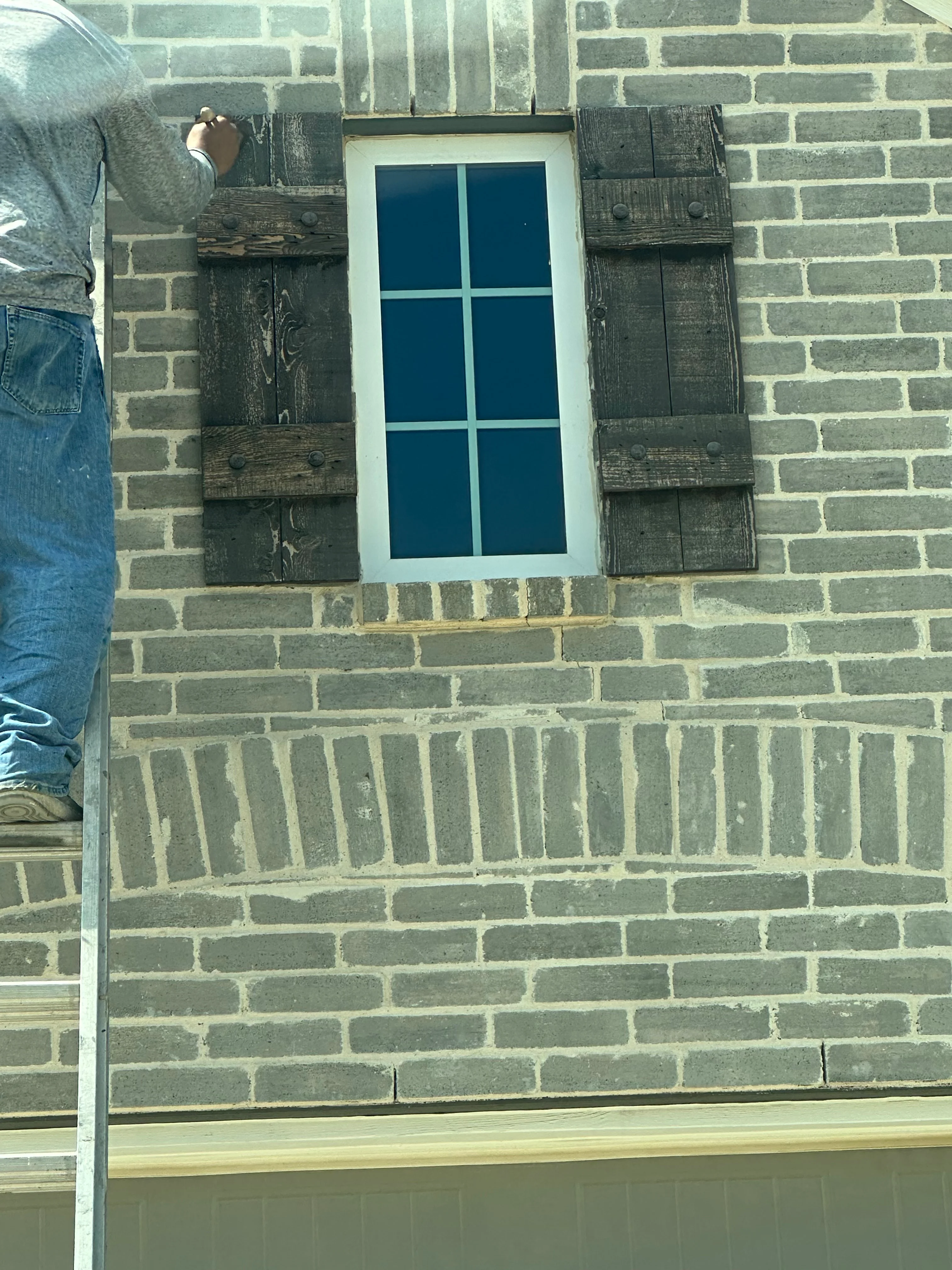 Weathered wood shutters installed on brick wall with 6-pane window and white trim