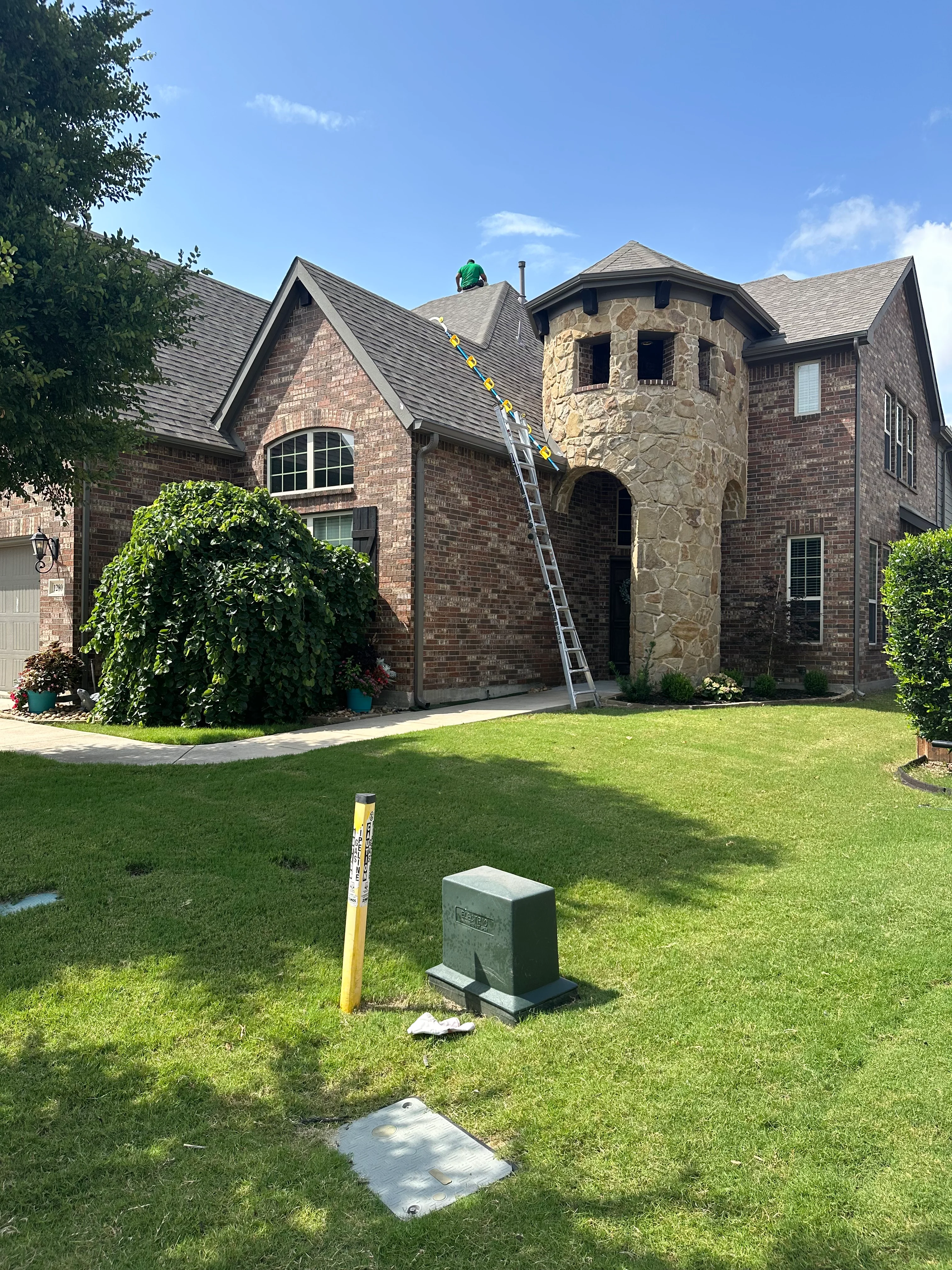 Two-story brick home with new asphalt shingle roof installation in progress on multiple roof planes